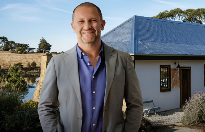 Anthony Burke wearing a blue shirt and grey blazer standing outside of a newly reroofed cottage