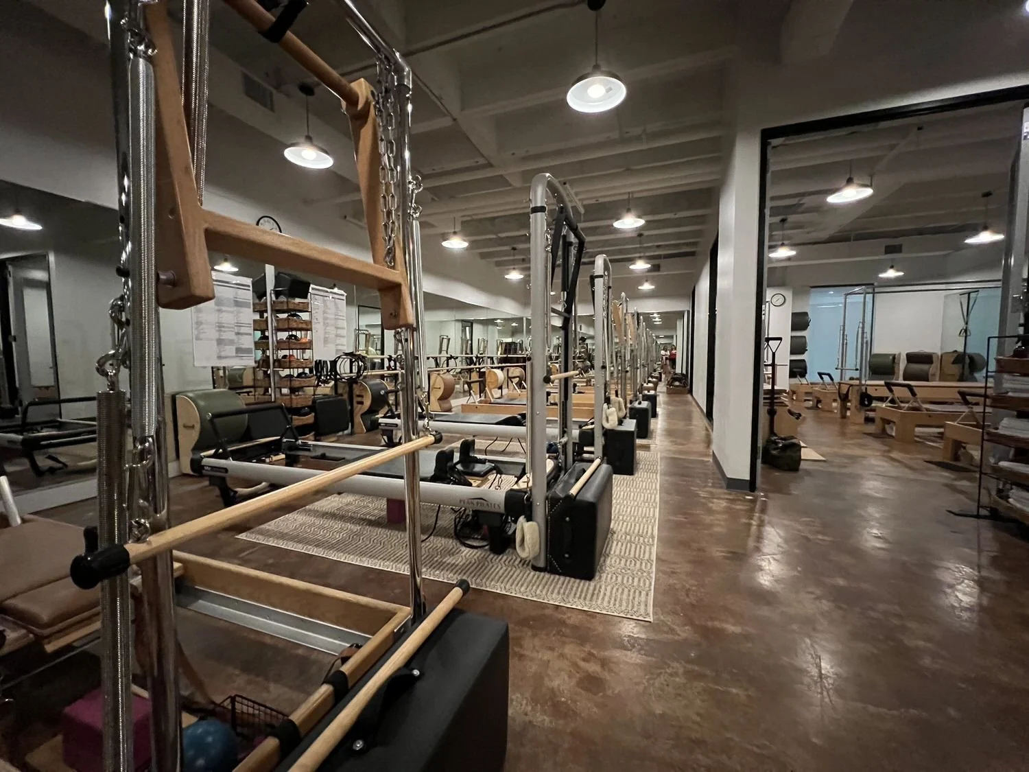 Pilates studio with reformer machines, wood and metal equipment, mirrors, and a polished wood floor.