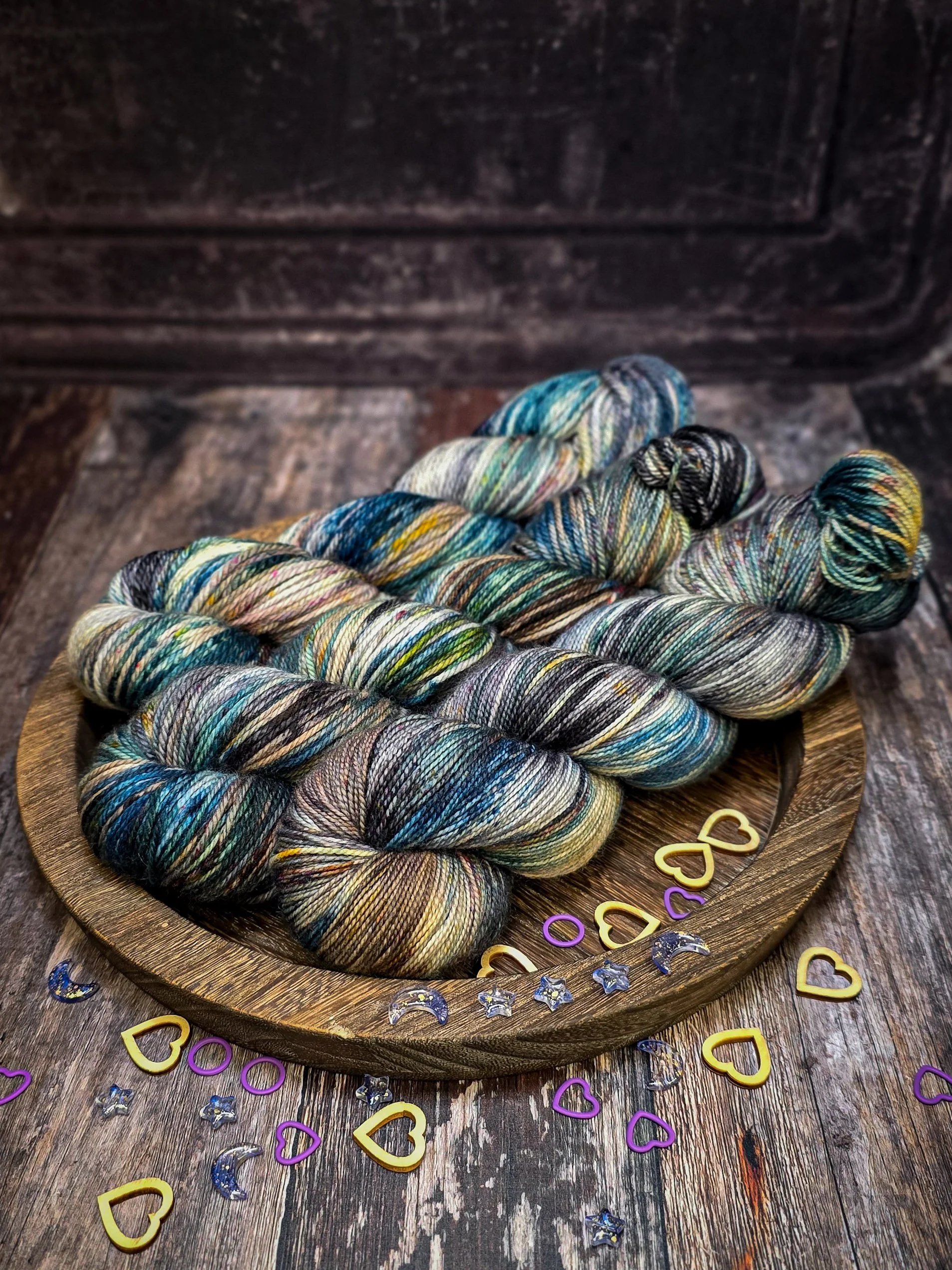 Colorful hand-dyed yarn skeins on a wooden plate with decorative moon, star, and heart shaped confetti.