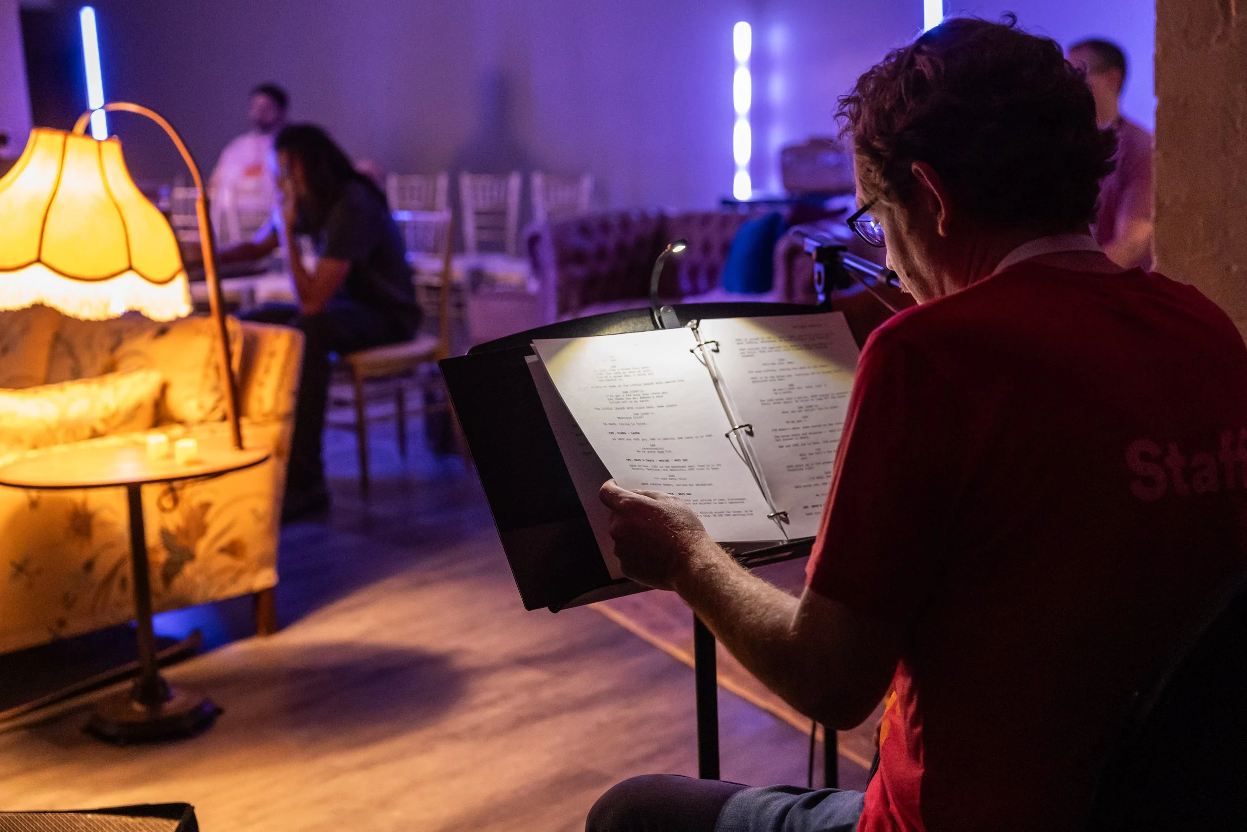 A person reading aloud a screenplay that he is looking at on a stand for the Screenplay Speakeasy program. Back turned to camera