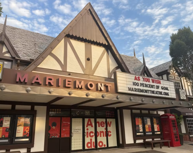 The marquee of the Mariemont Theatre with a sign reading 'As you wish, 100 percent of goal, mariemonttheatre.org,' and a red phone booth outside.