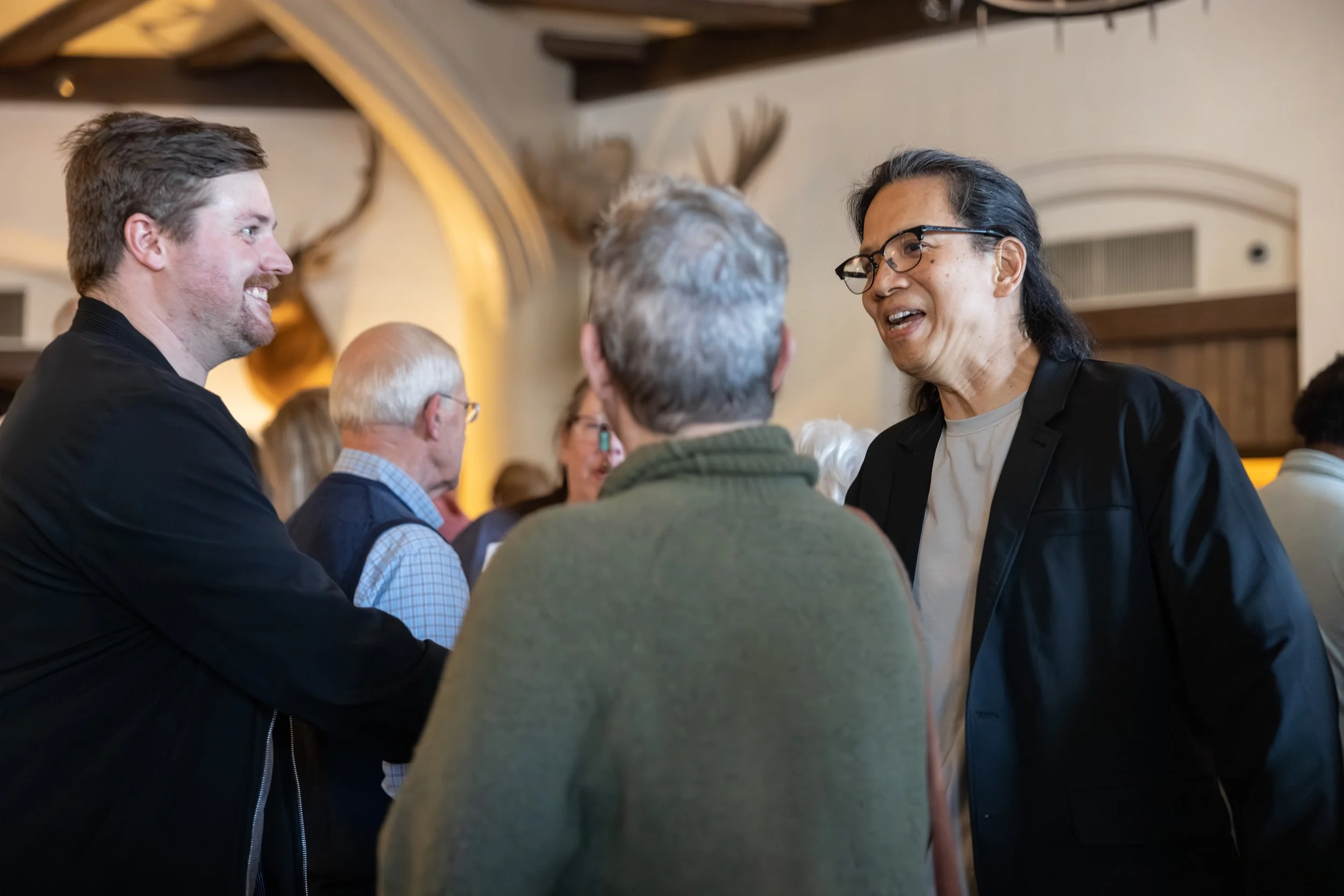 A group of three people in focus amongst a crowd smiling, talking, and shaking hands. Image links to the Mariemont Theatre Community Survey.