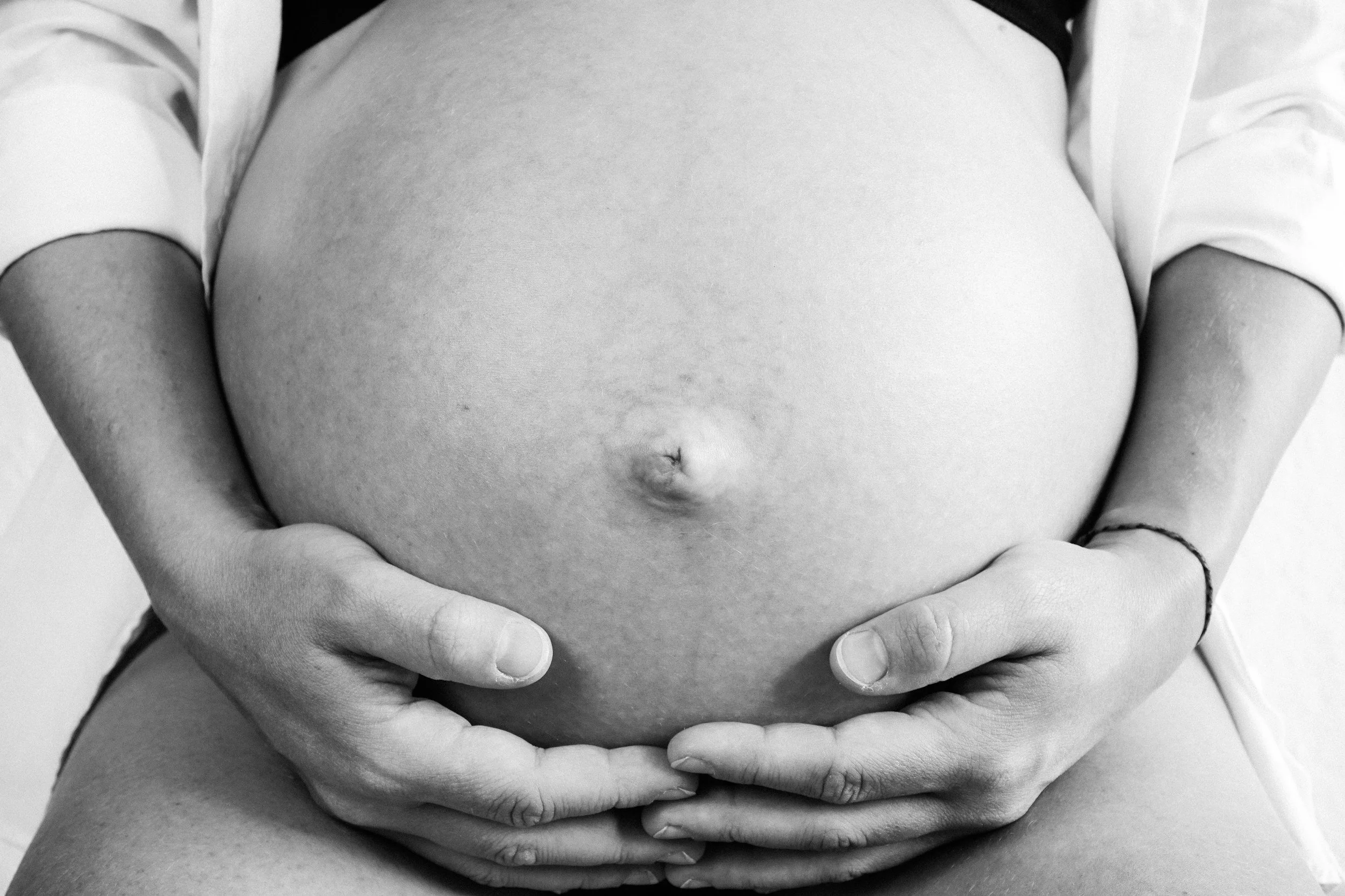 Une femme enceinte tenant son ventre par les mains en position assise ou allongée.