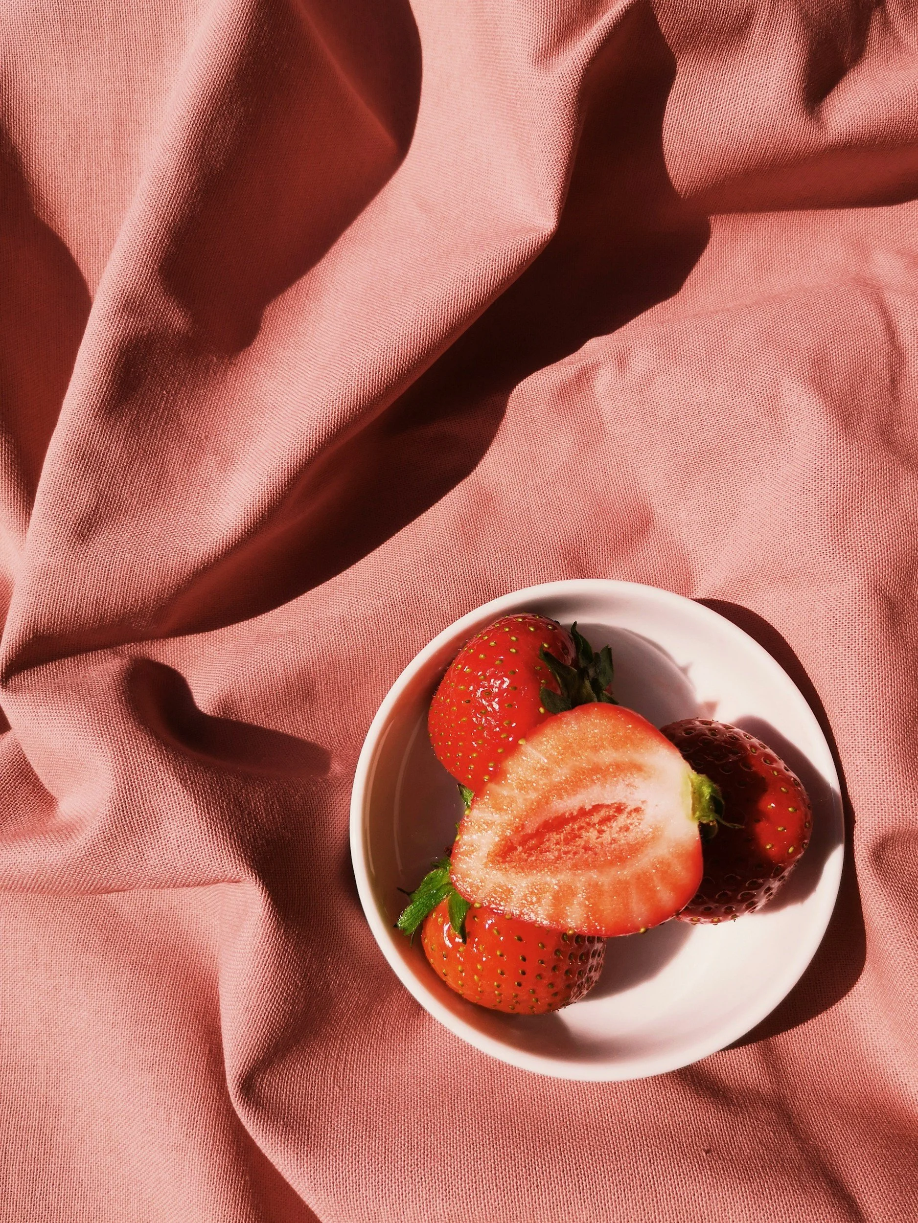 Fraises entières et coupées dans un bol blanc sur un tissu rose