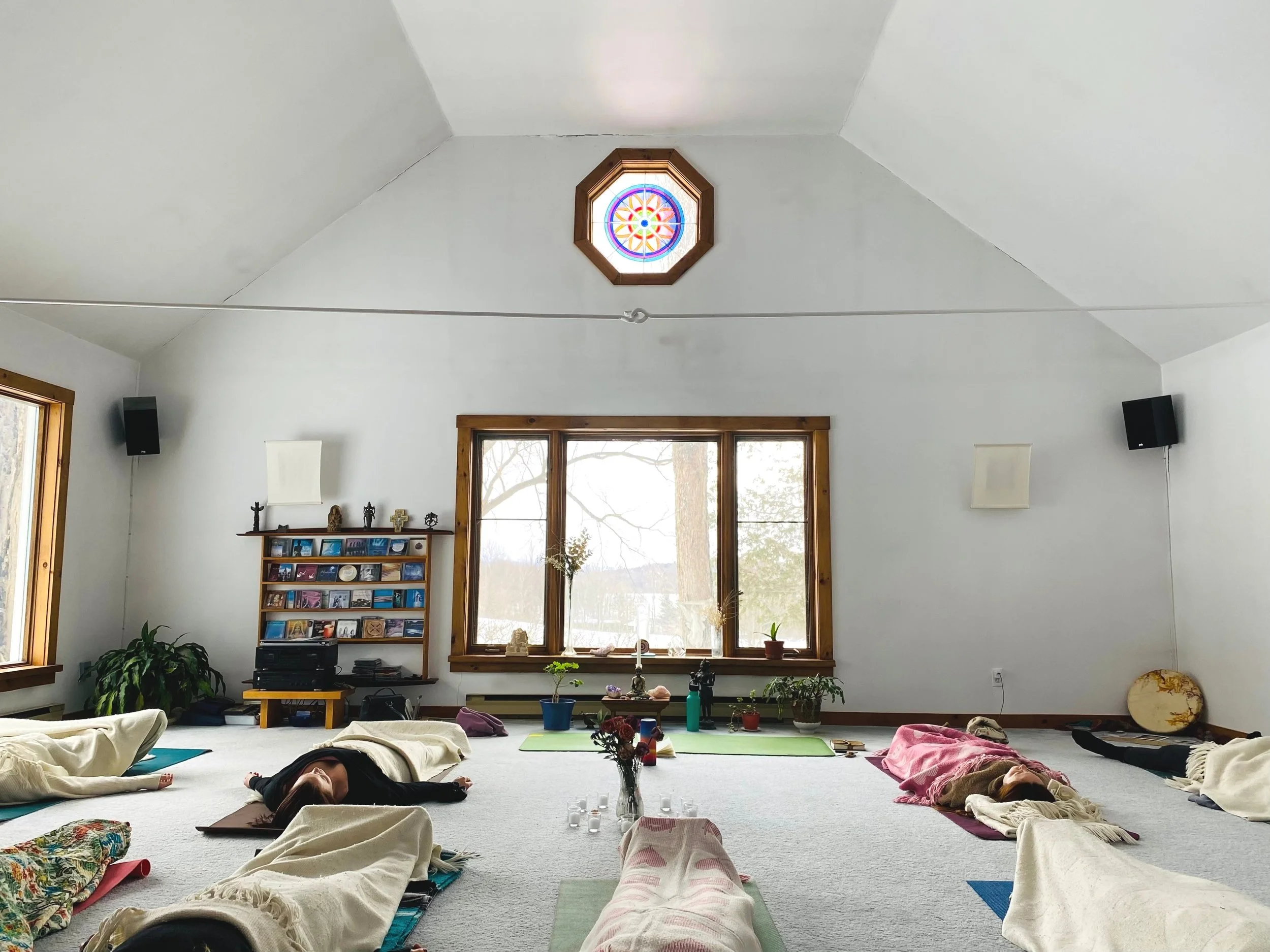 Pratique de yoga, couvertures et briques alignés sur le sol en bois, éclairée par la lumière du soleil, plafond en bois avec des lampes circulaires suspendues.