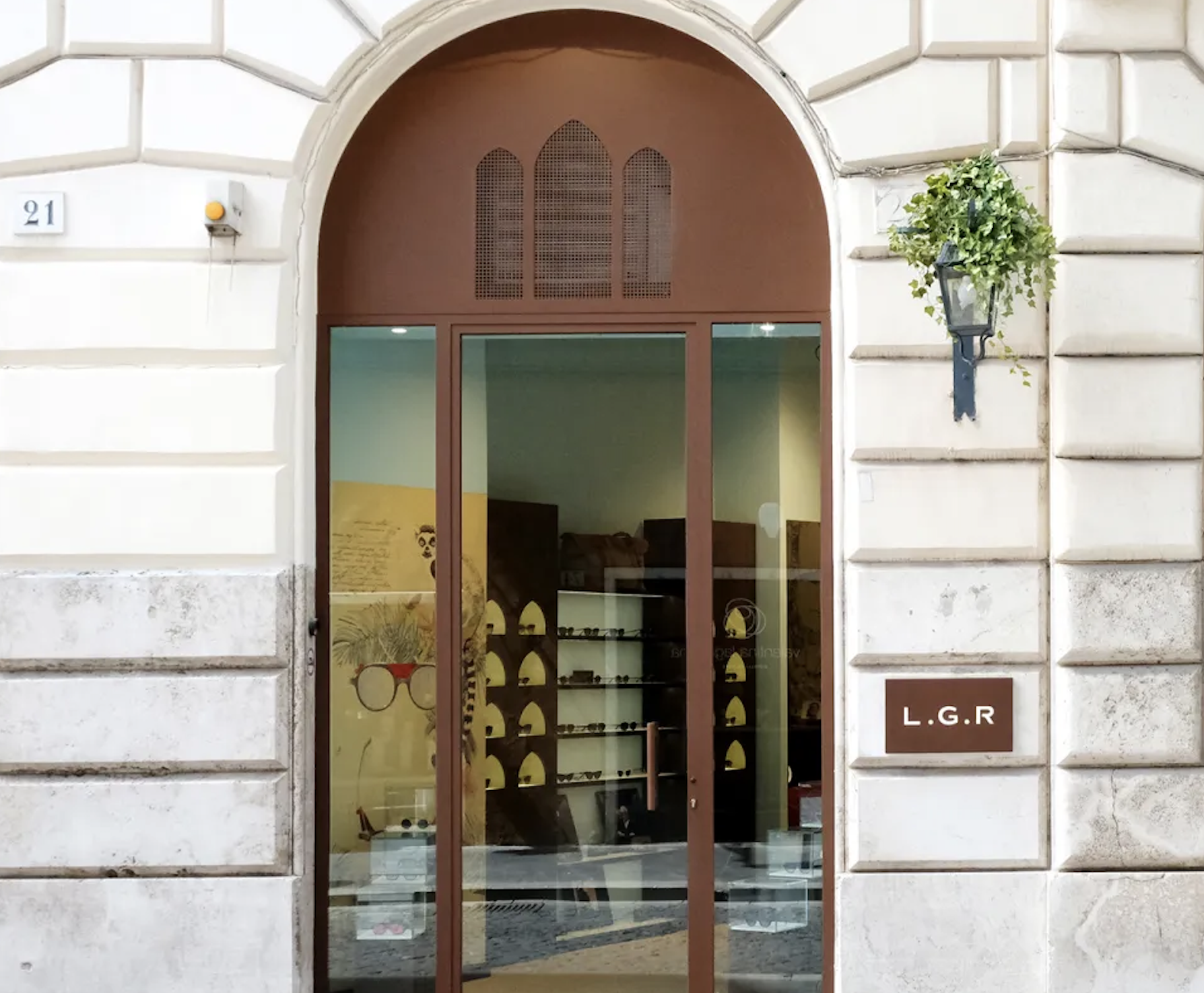 Façade d'une boutique optique avec une porte en verre, un mur en pierre blanche, une petite lampe et un panneau avec les initiales L.G.R.