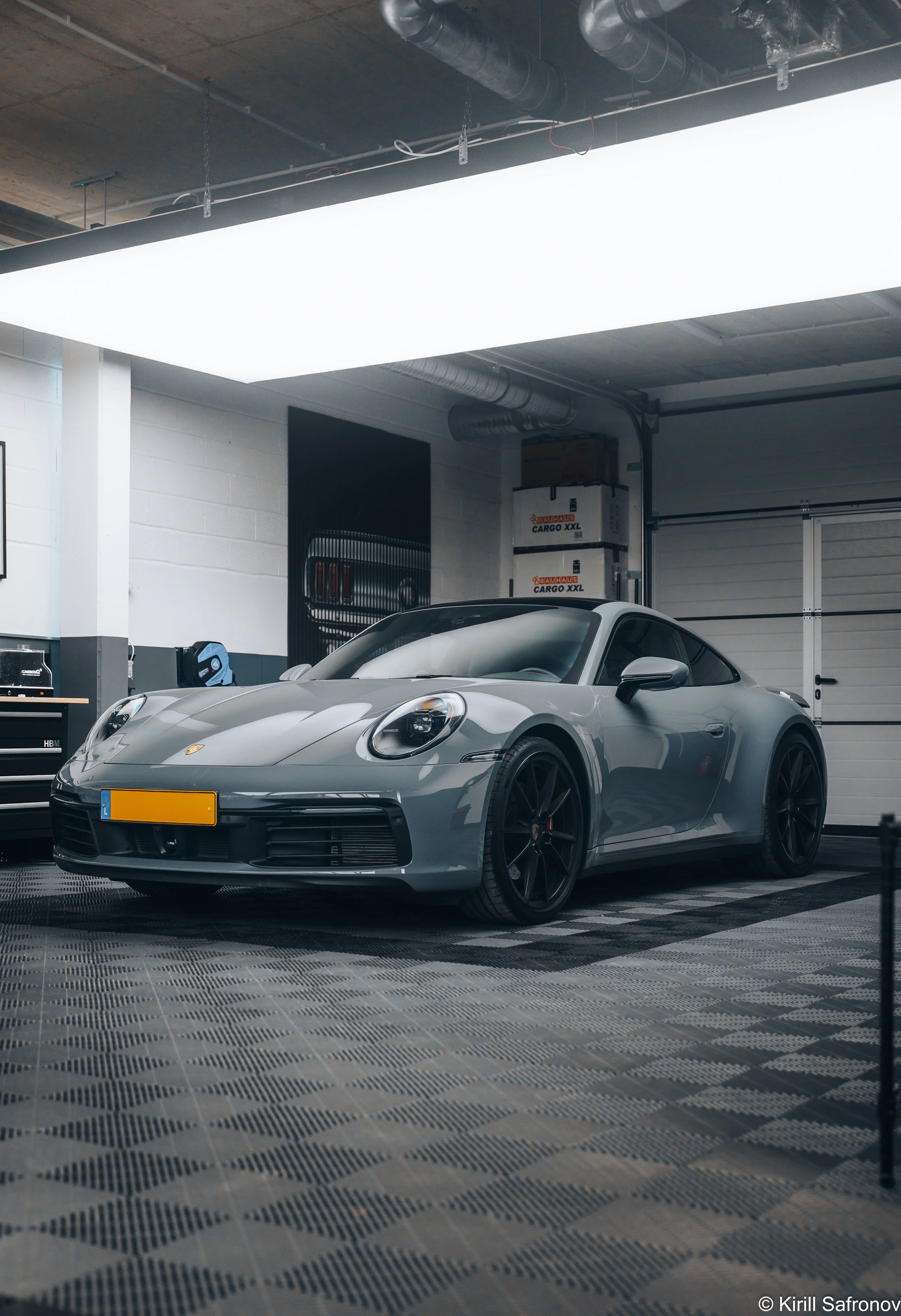 Gray Porsche 911 Carrera 4S in a modern luxury garage, featuring a black-and-white tiled floor, white walls, and a premium automotive showroom atmosphere.