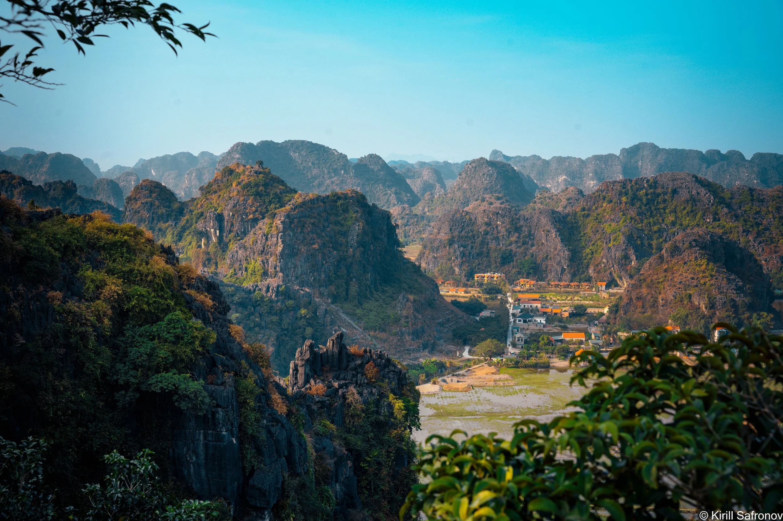 Photo of Ninh Binh, Vietnam, featuring dramatic karst mountains, traditional countryside villages, lush rice fields, and a clear blue sky.
