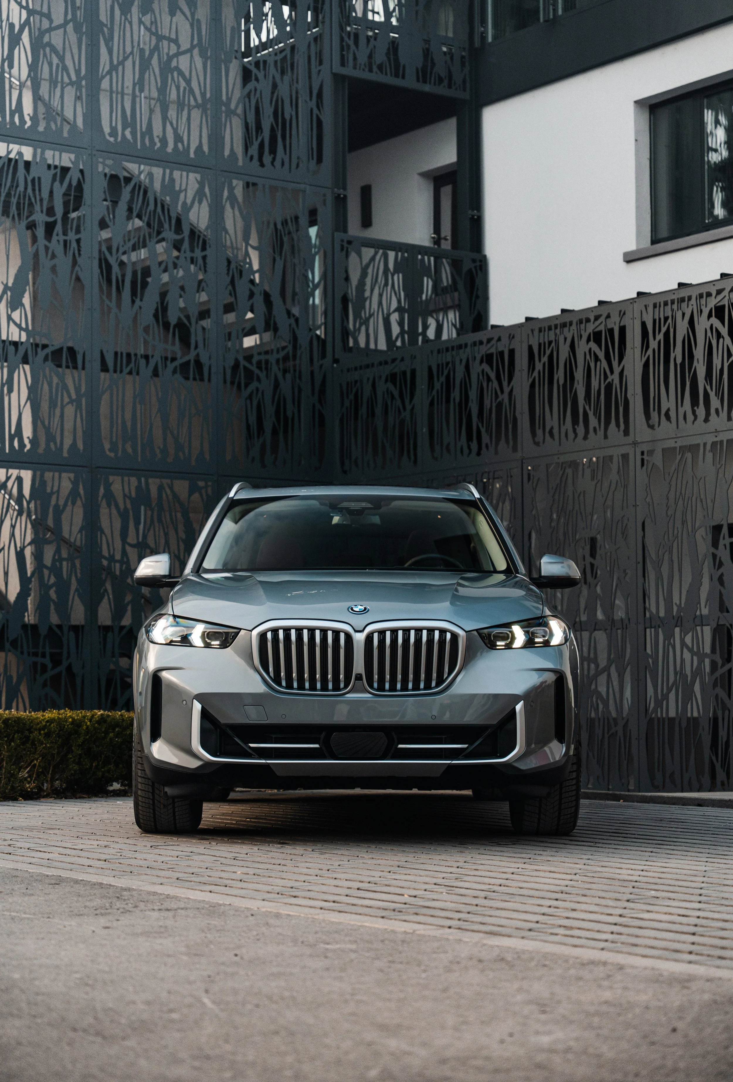 Photo of a dark gray BMW X5 parked in front of a modern building with a black metal mesh architectural facade.