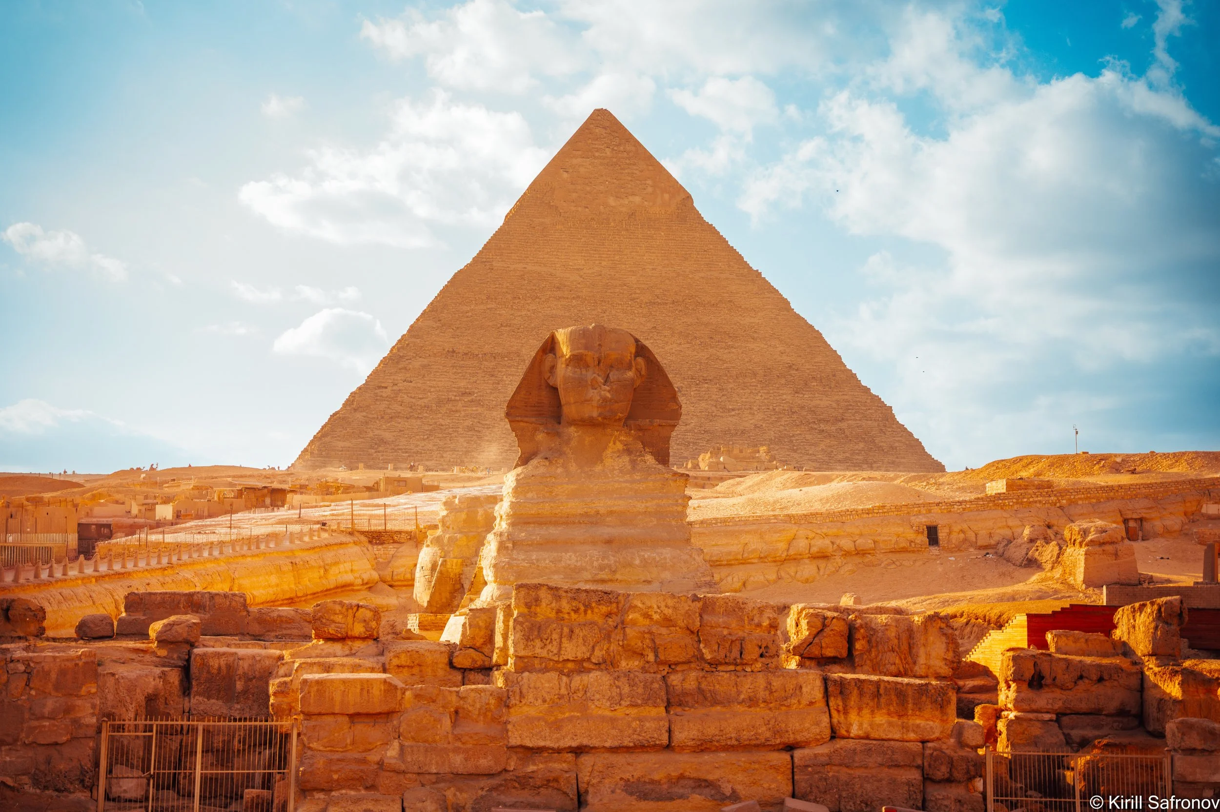 Photo of the Great Pyramid of Khufu and the Great Sphinx of Giza in Egypt, with the ancient Giza Plateau monuments under a blue sky with clouds.