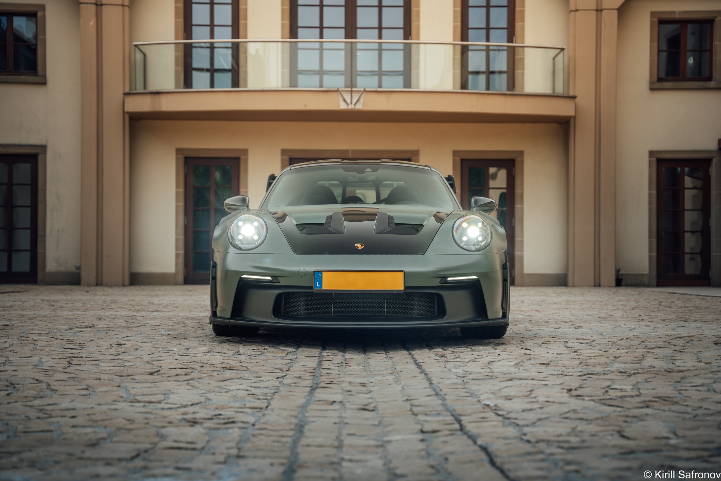 Dark green Porsche 911 GT3 RS photographed from the front, parked on a cobblestone street in front of an elegant classic-style house.