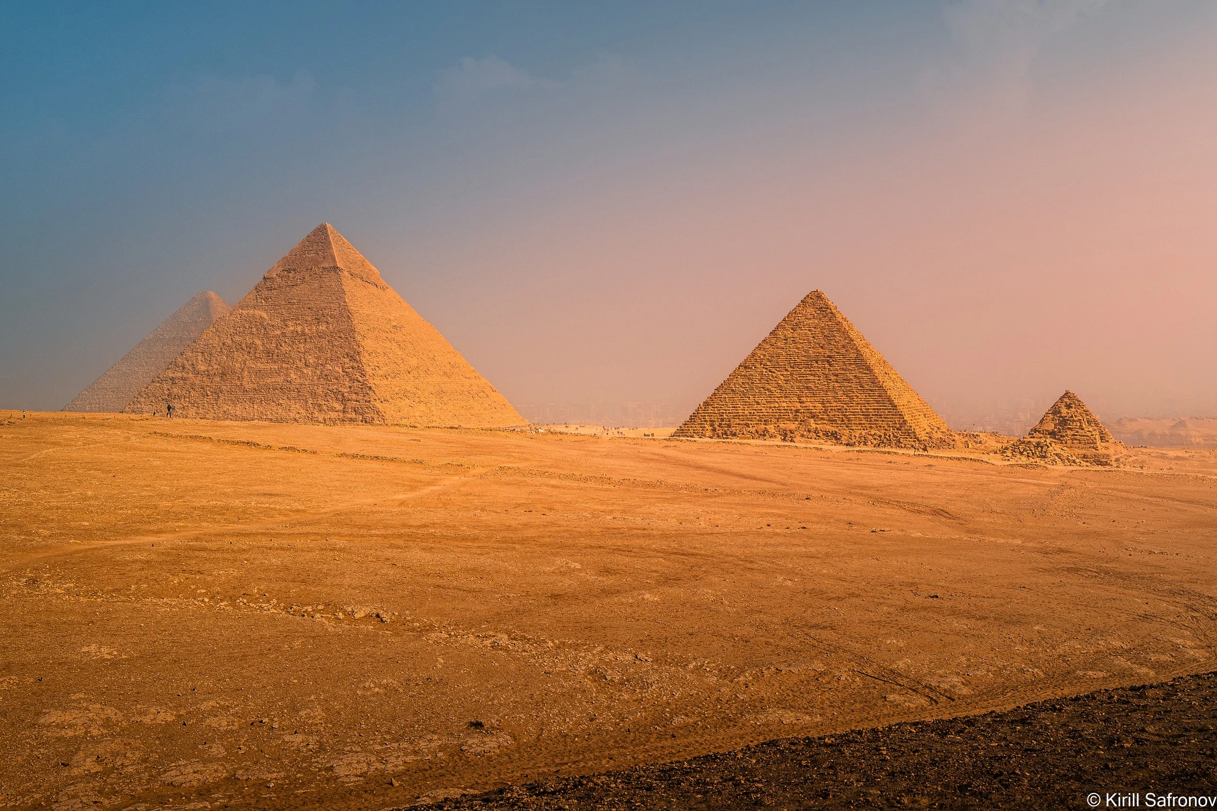Photo of the Pyramids of Giza in the Egyptian desert at sunset, with a clear sky and warm golden light.