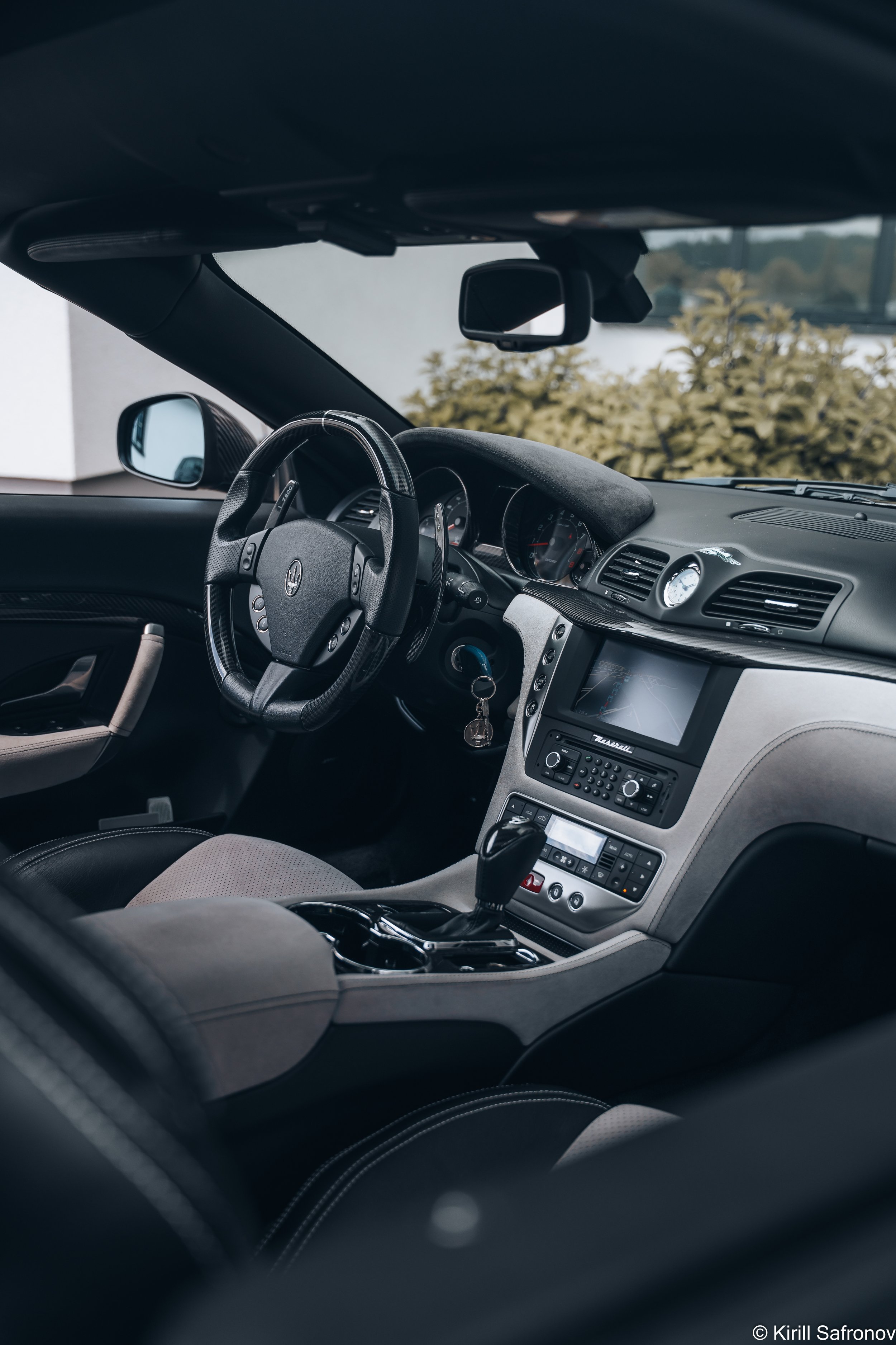 Photo of a Maserati GranTurismo interior featuring a leather dashboard, leather steering wheel, center console with display screen, and gear shift, captured from inside the luxury sports car.