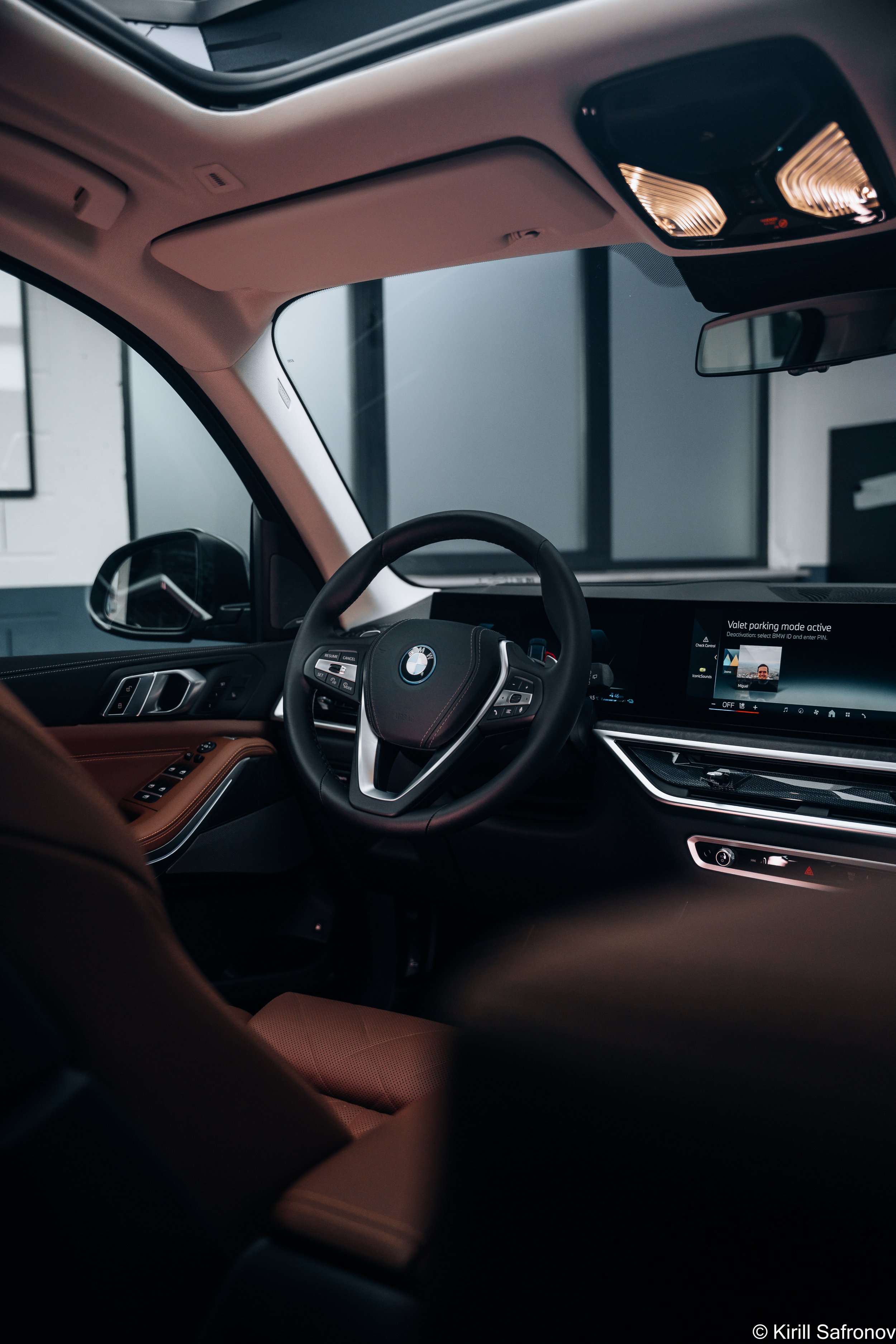 Photo of a BMW X5 lux interior dashboard, steering wheel, and rearview mirror, with a digital screen showing active parking mode.