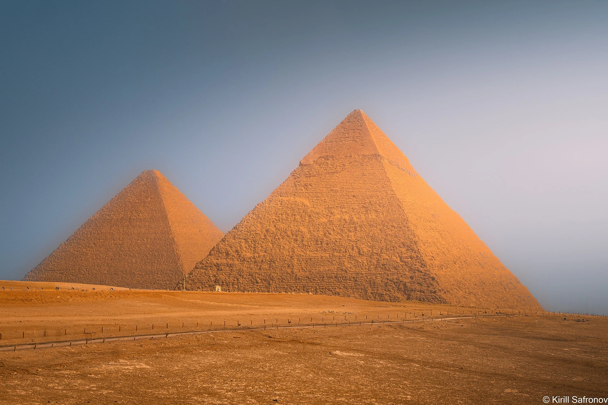 Photo of three large stone pyramids in a sunny desert landscape under a clear, cloudless blue sky.