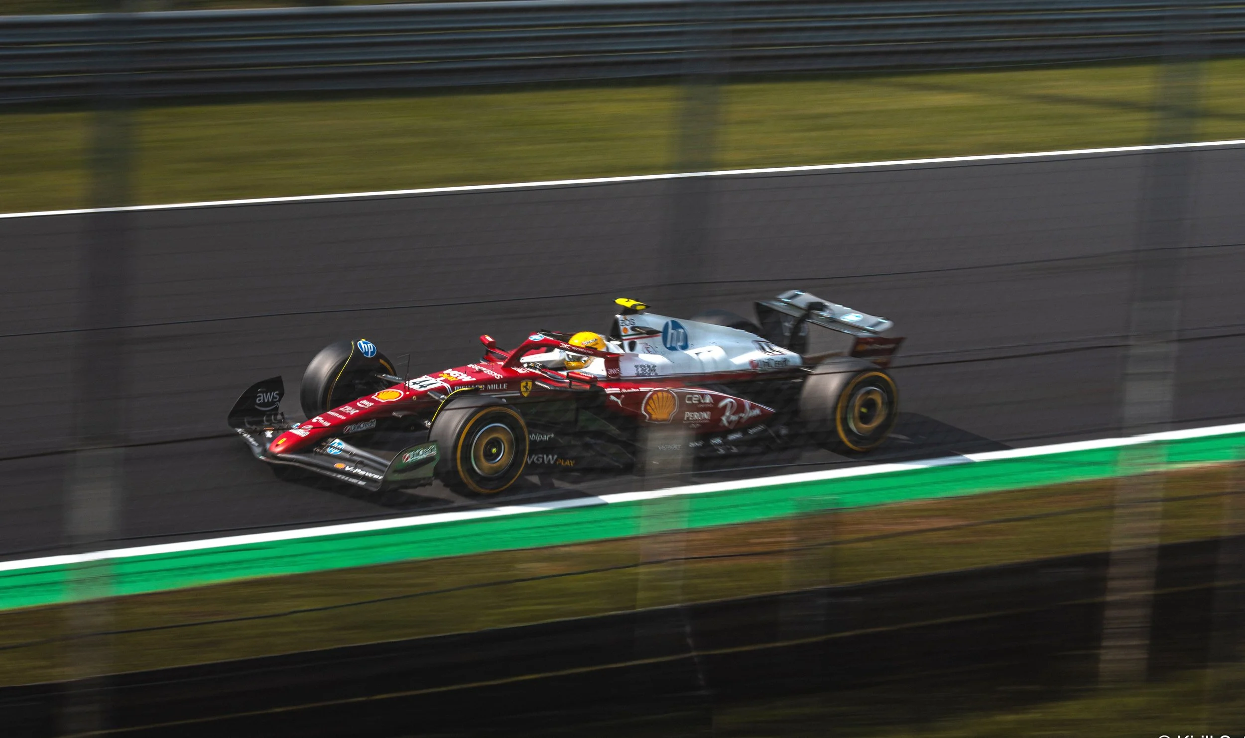 Photo of Lewis Hamilton driving a red and white Ferrari Formula 1 car at high speed on the Monza race circuit during the Italian Grand Prix, wearing a yellow helmet.