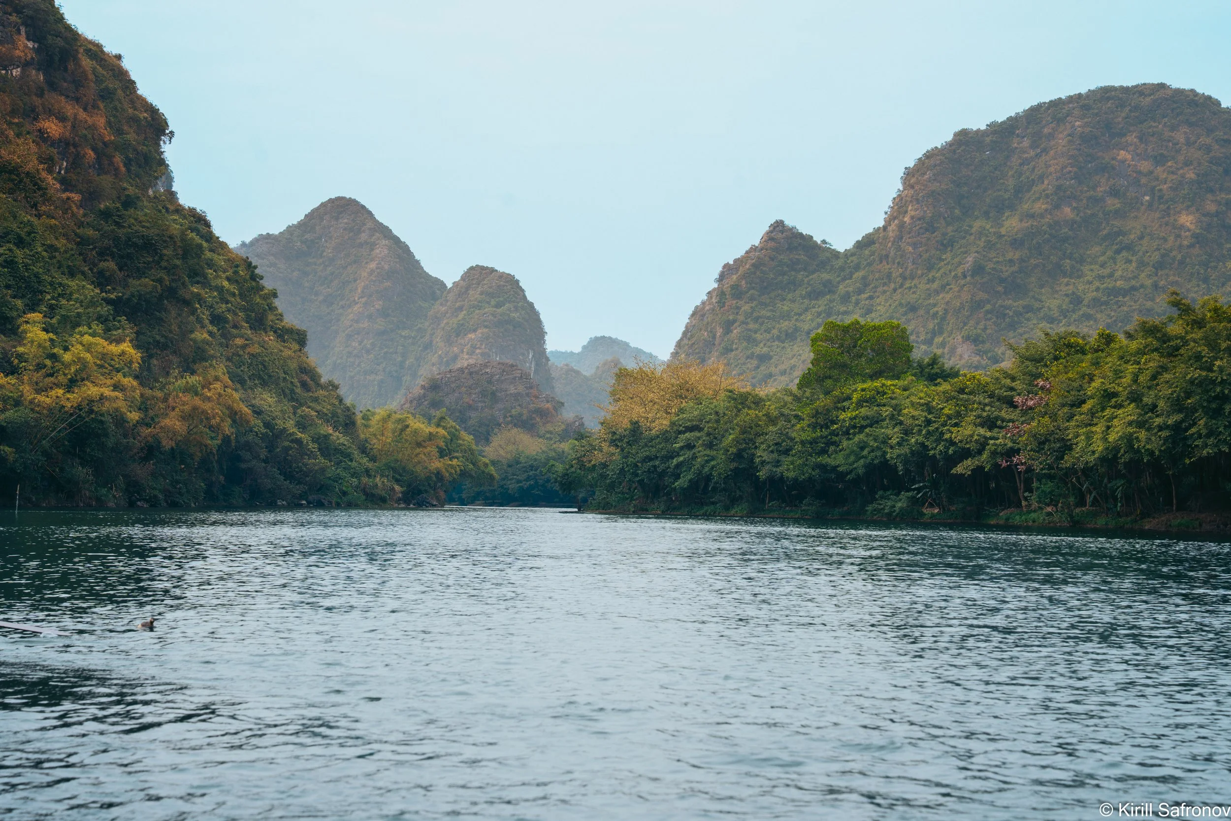 Photo of a peaceful river landscape in Ninh Binh, Vietnam, with lush green mountains, tropical nature, and a clear blue sky, capturing the scenic beauty of northern Vietnam.