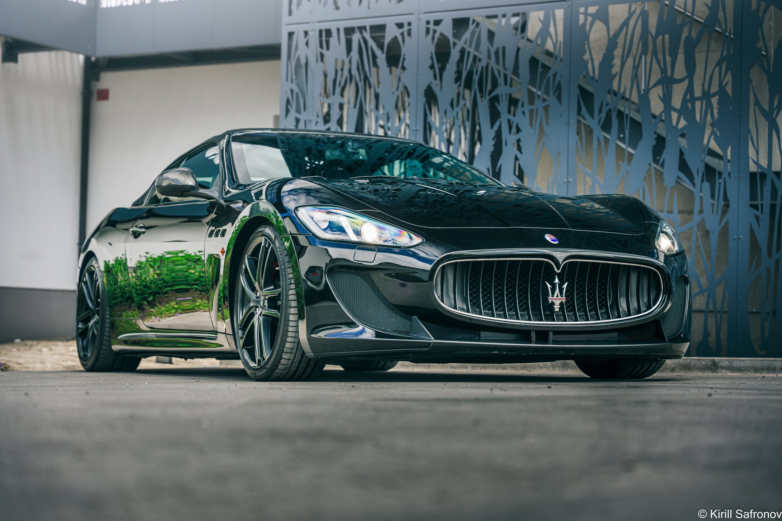 photo of Elegant black Maserati GranTurismo parked in front of a contemporary building façade featuring intricate cut-out metal patterns and modern architectural design.