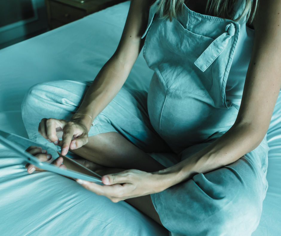 Person sitting on a bed using a tablet, wearing a light blue apron and light blue pajamas.