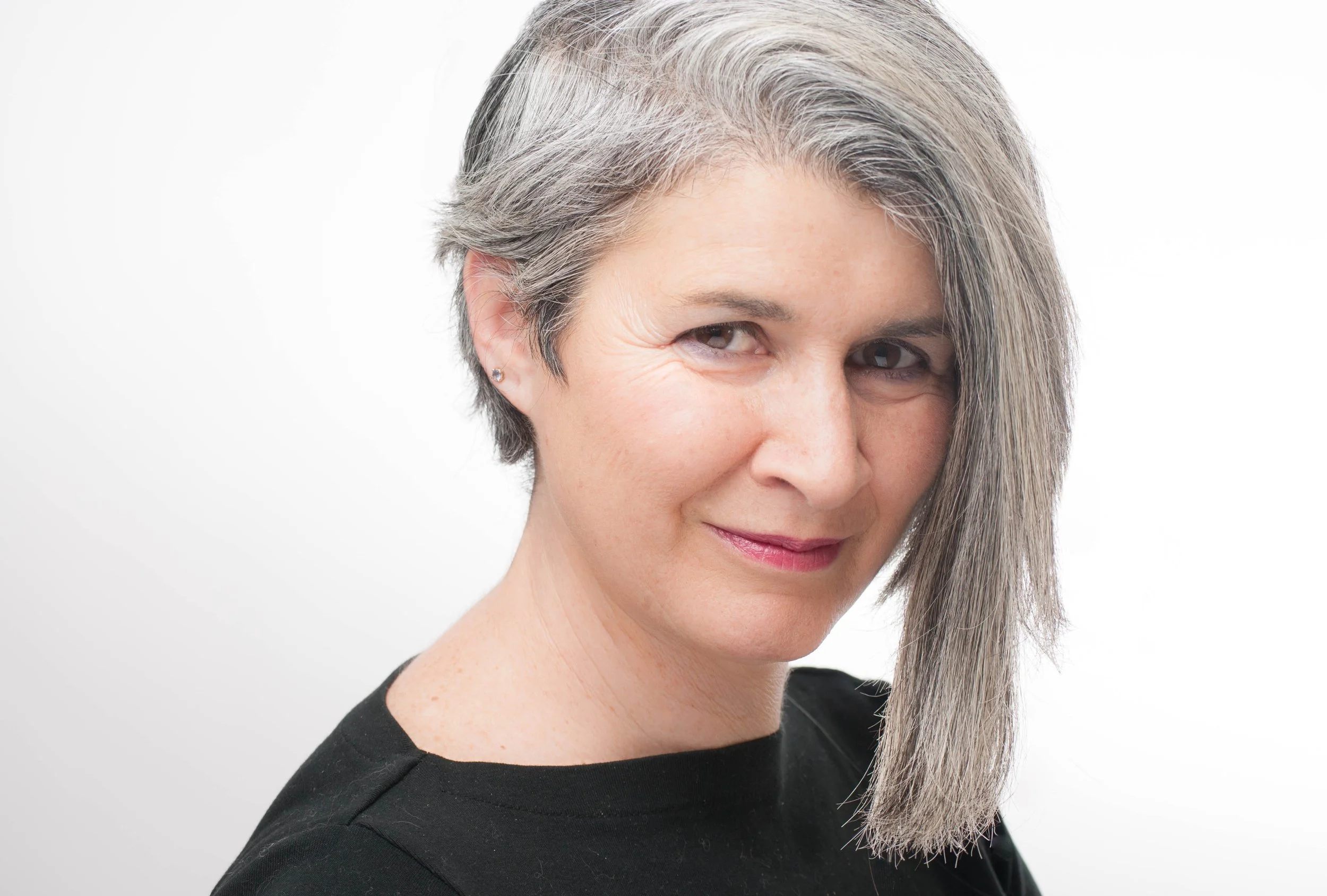 A woman with short gray hair, smiling slightly, wearing a black top, against a plain white background.