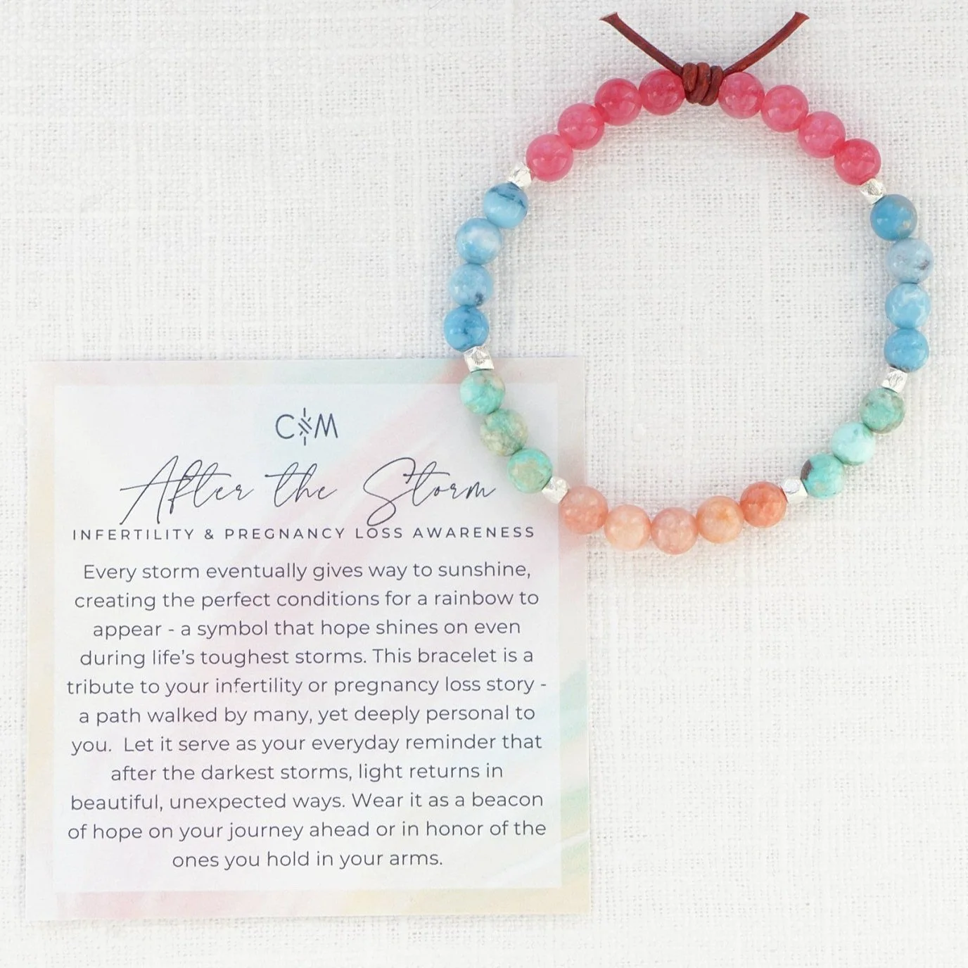 Colorful beaded bracelet with pink, blue, green, and peach beads, accompanied by a card titled 'After the Storm' about infertility and pregnancy loss awareness.