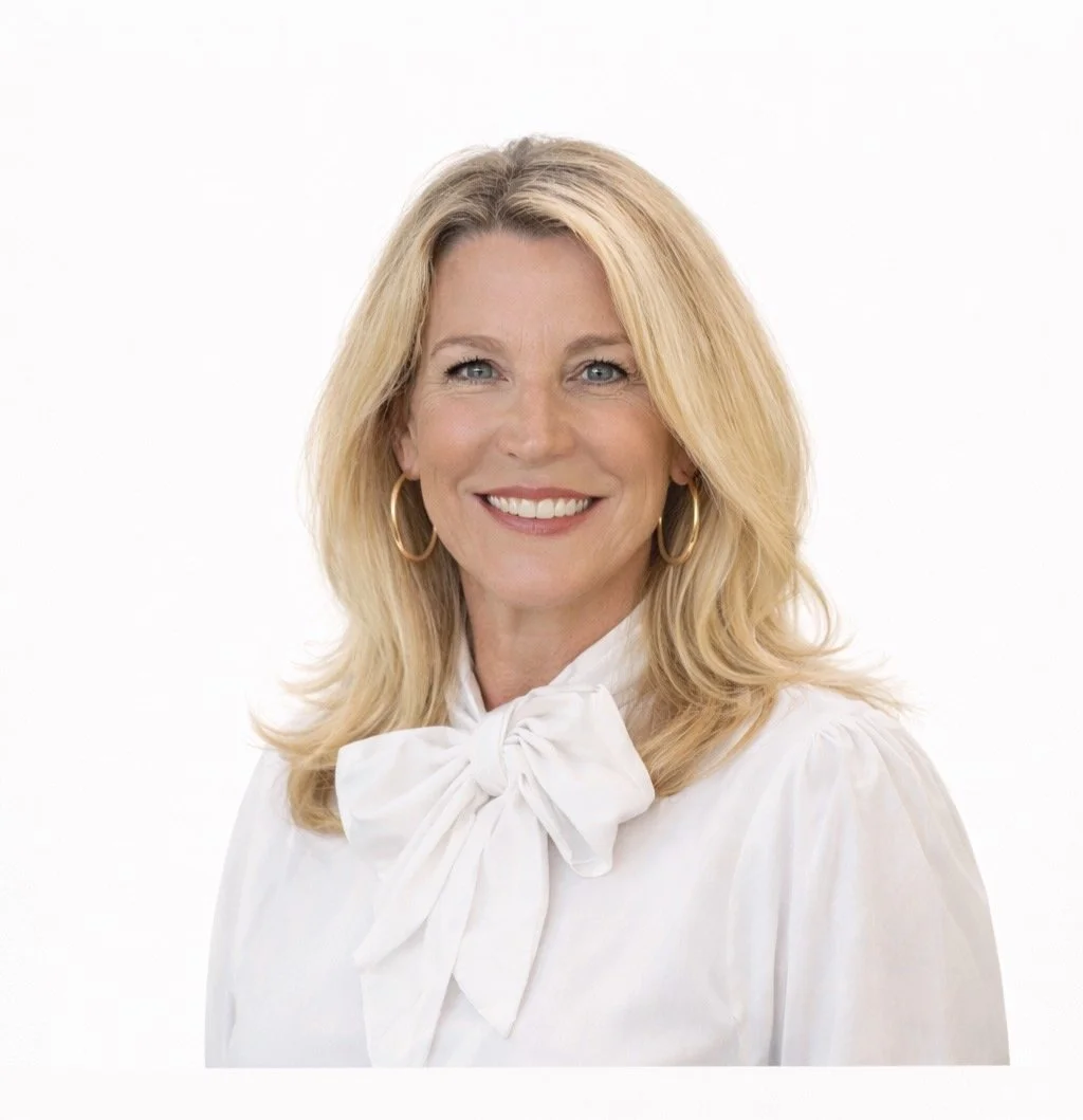 A smiling woman with shoulder-length blonde hair wearing gold hoop earrings and a white blouse with a bow at the neck against a white background.