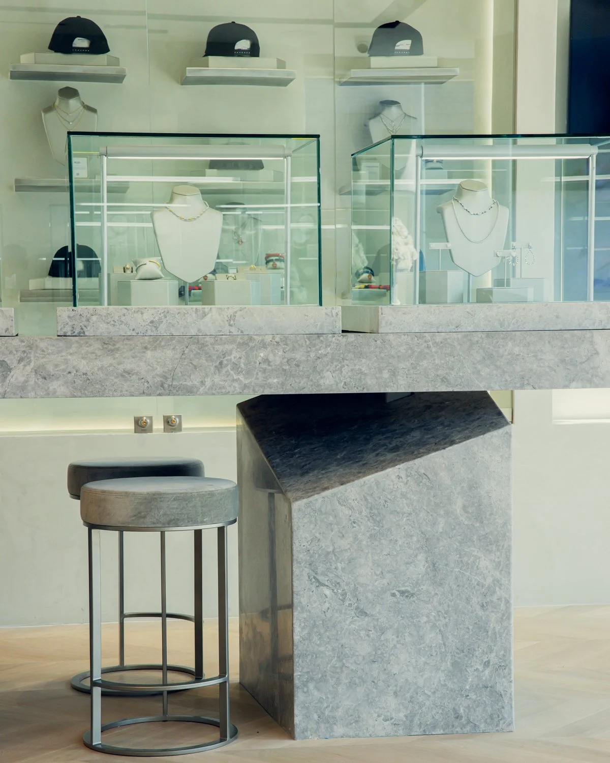 Night view of a city street corner with a well-lit storefront, pedestrians, parked cars, and cityscape in the background.