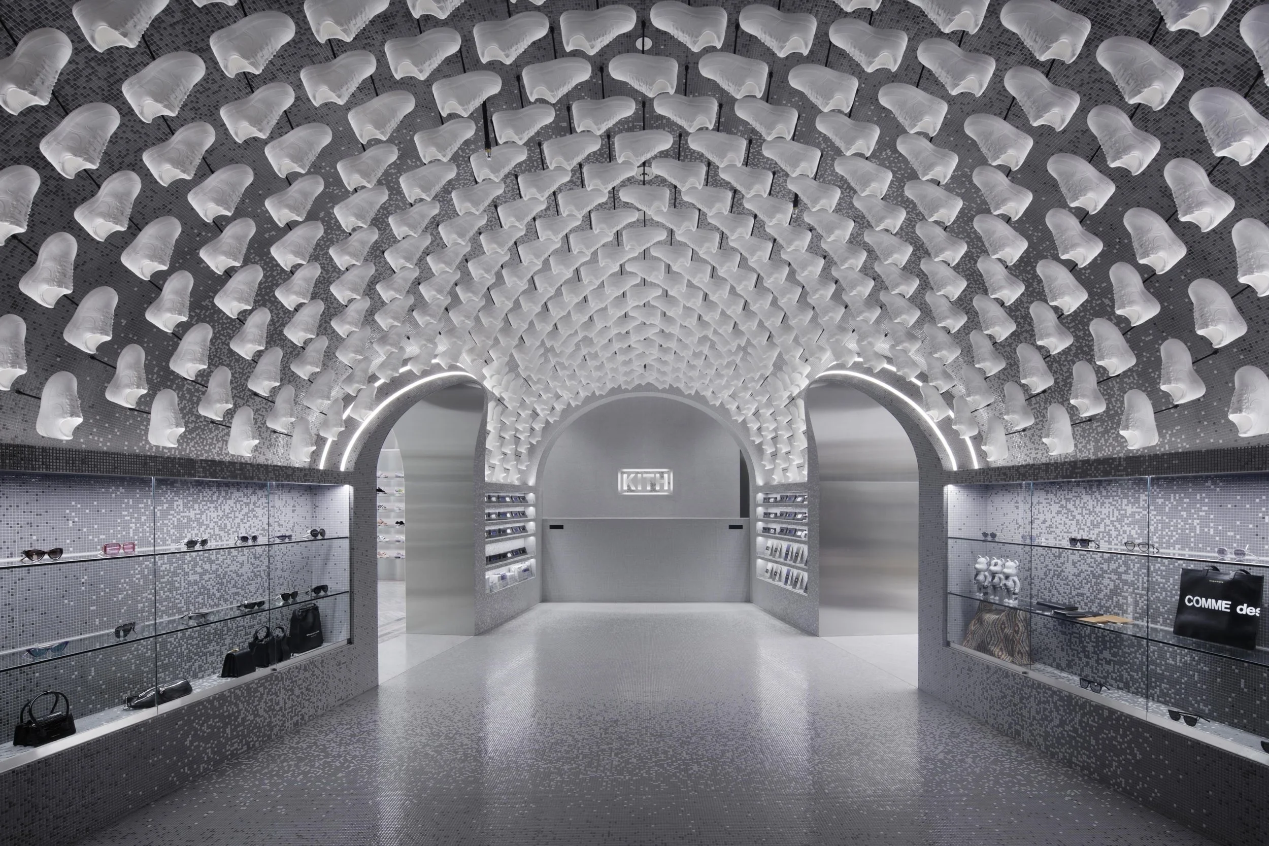 Modern sneaker store with white sneakers displayed on an arched ceiling and shelves, featuring a metallic entrance, illuminated with LED lighting.