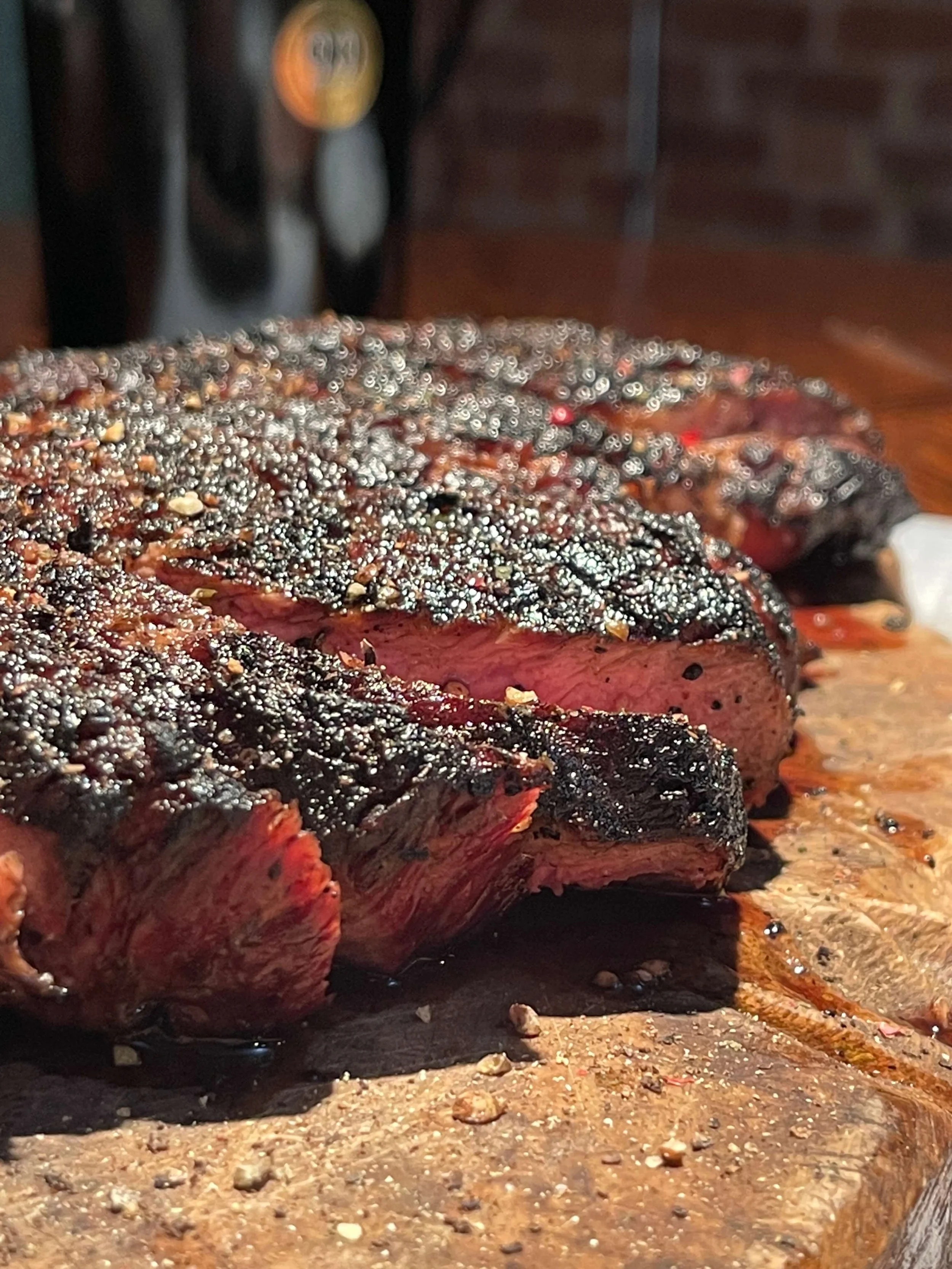Close-up of a perfectly cooked steak with a charred, peppercorn-crusted crust, resting on a wooden cutting board.