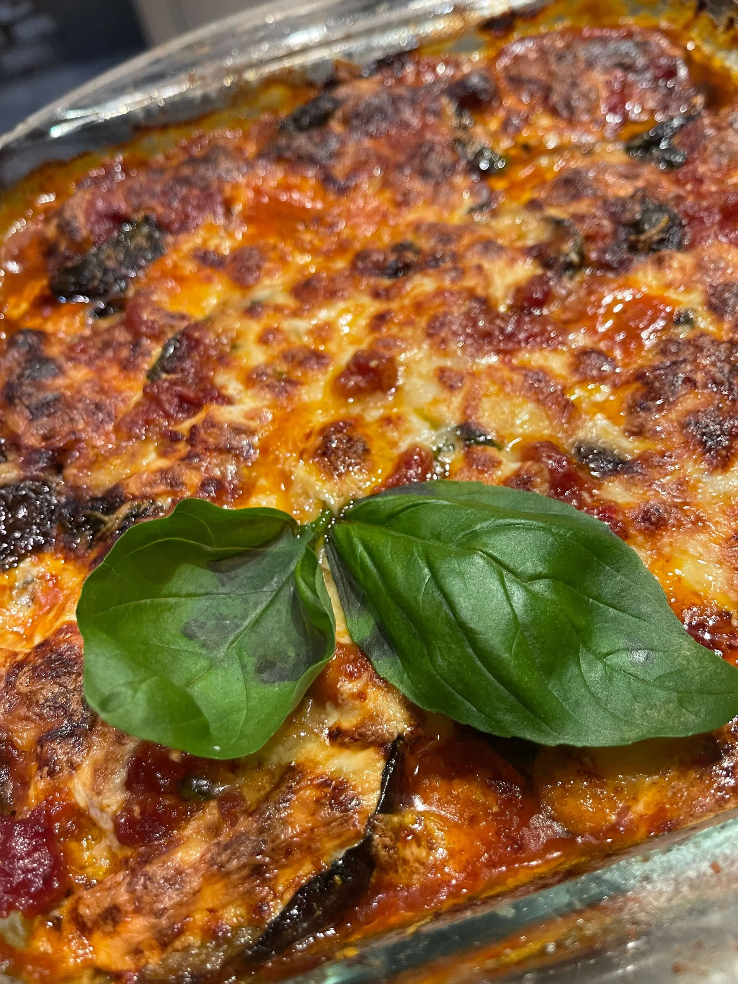 Baked Italian casserole topped with melted cheese, meat sauce, and fresh basil leaves.