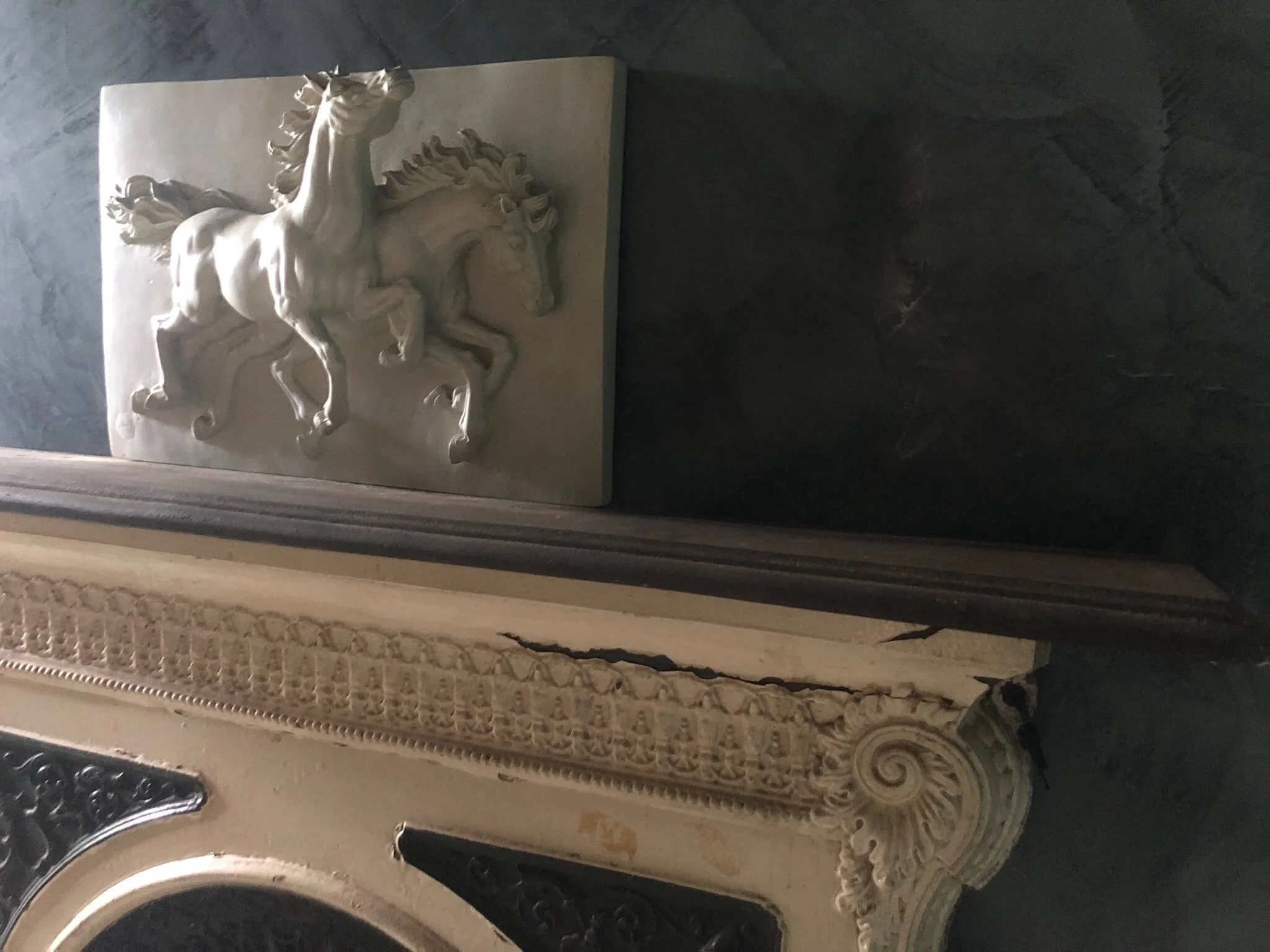 A white marble sculpture of a rearing horse atop a rectangular base, positioned against a dark wall.