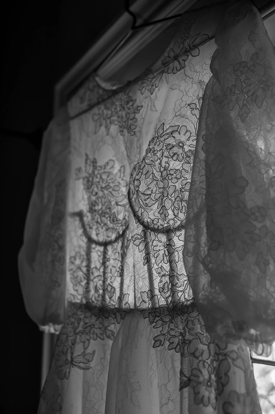 Close-up of lace curtains with floral embroidery hanging by a window.