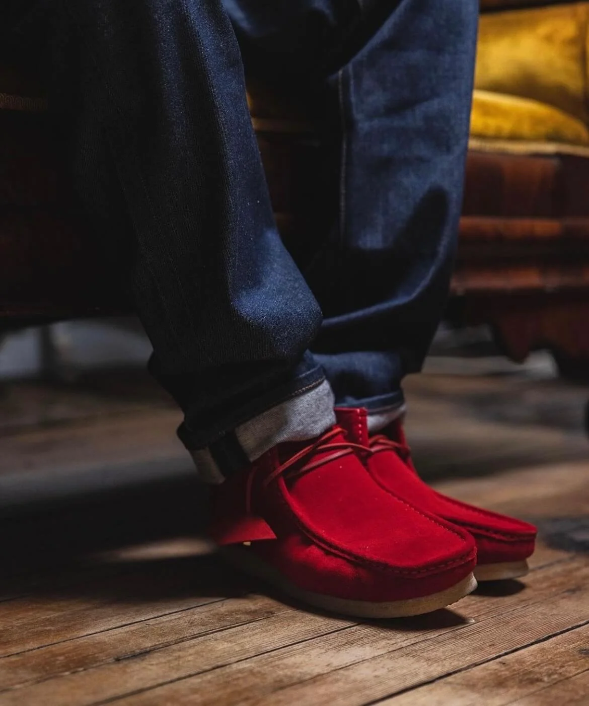 Close-up of a person sitting on a wooden bench, wearing blue jeans and bright red shoes.