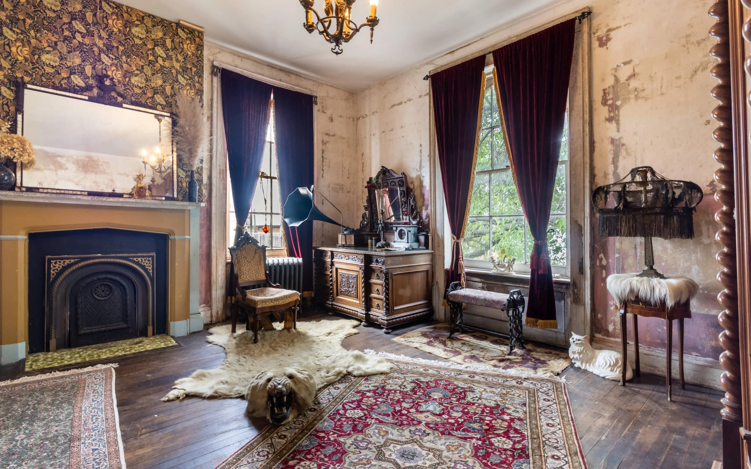 Antique living room with vintage furniture, ornate mirror, Victorian-style curtains, animal sculptures, large windows showing greenery, and a roaring lion rug.