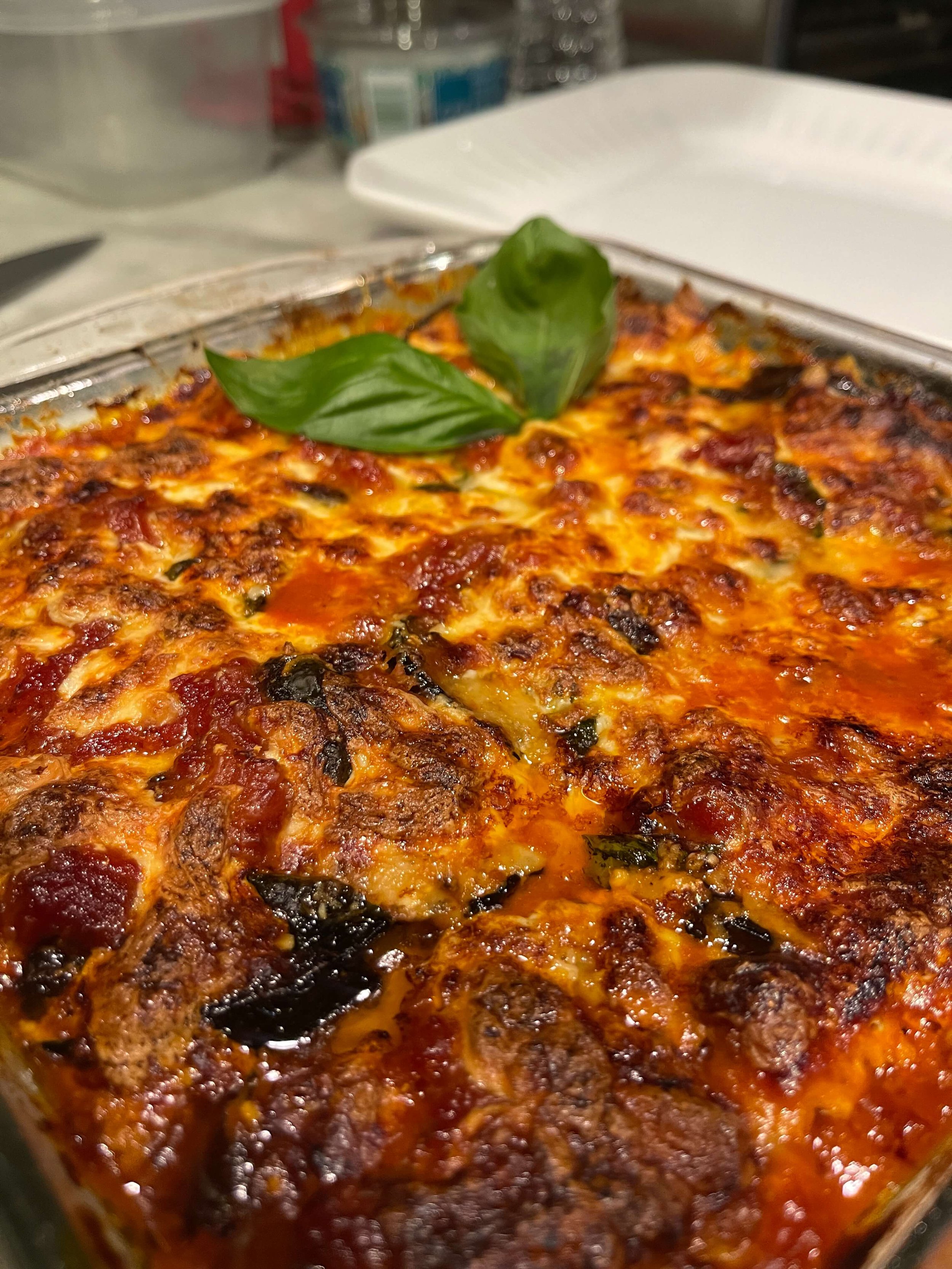 Baked meat lasagna with cheese and basil garnish in a glass dish.