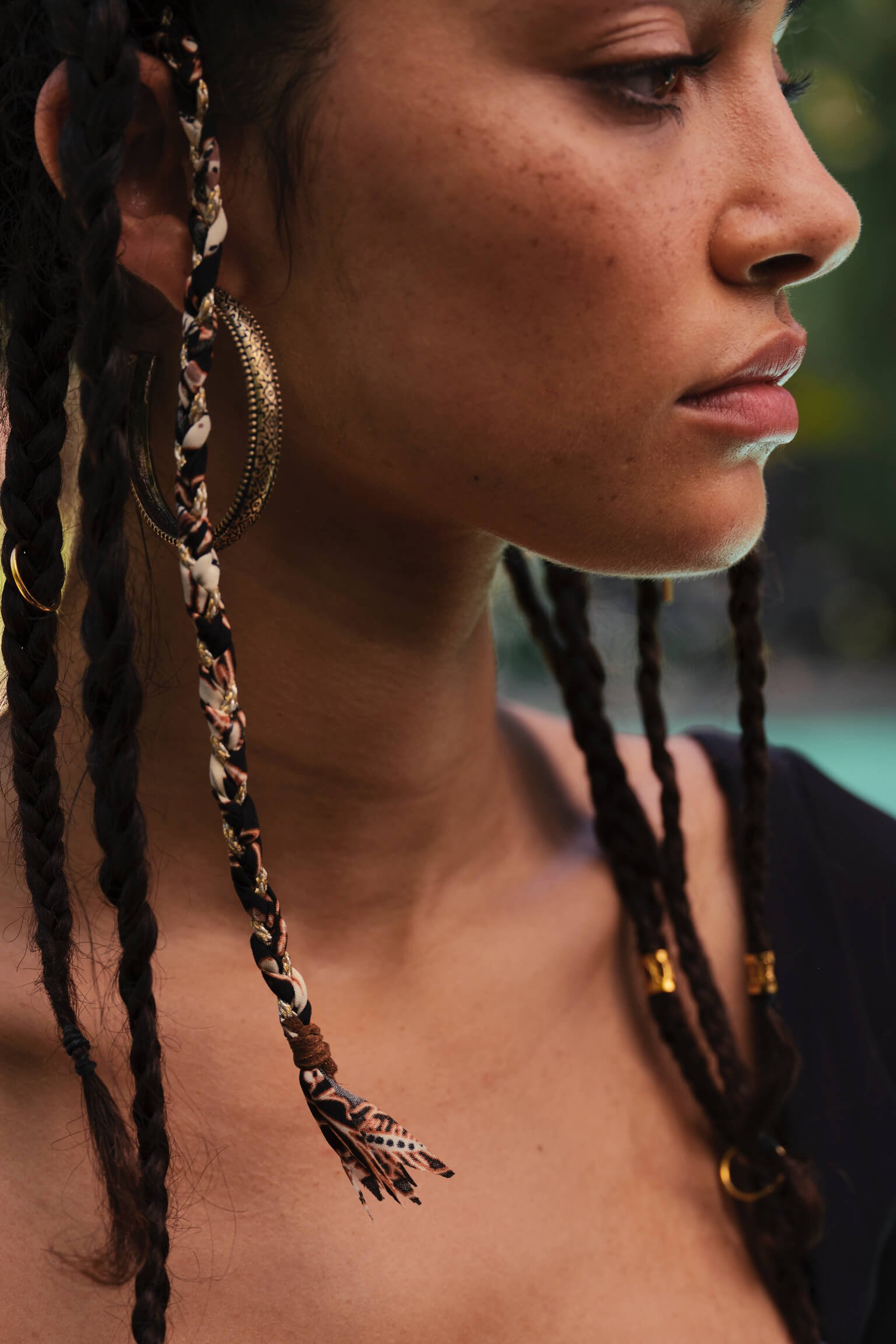 Close-up of a woman's face and shoulder showing her jewelry and braids.