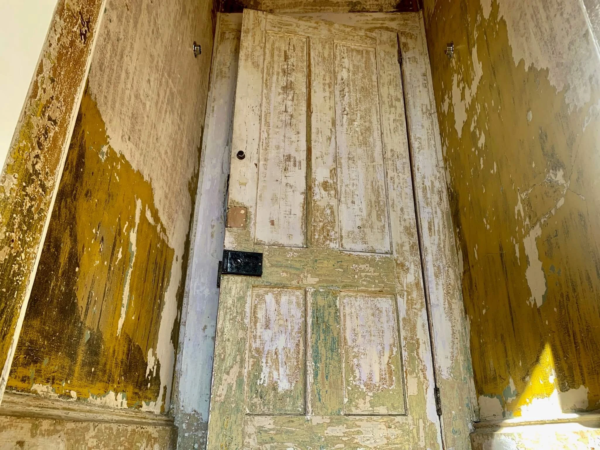 Old wooden door with peeling paint, surrounded by worn yellow painted walls.