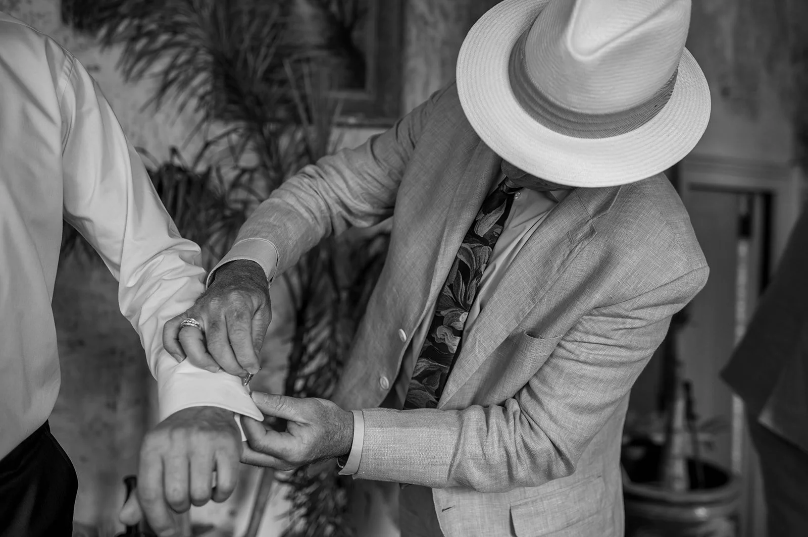 A man in a light-colored suit and wide-brimmed hat adjusting a woman's cuff in a black and white photograph.