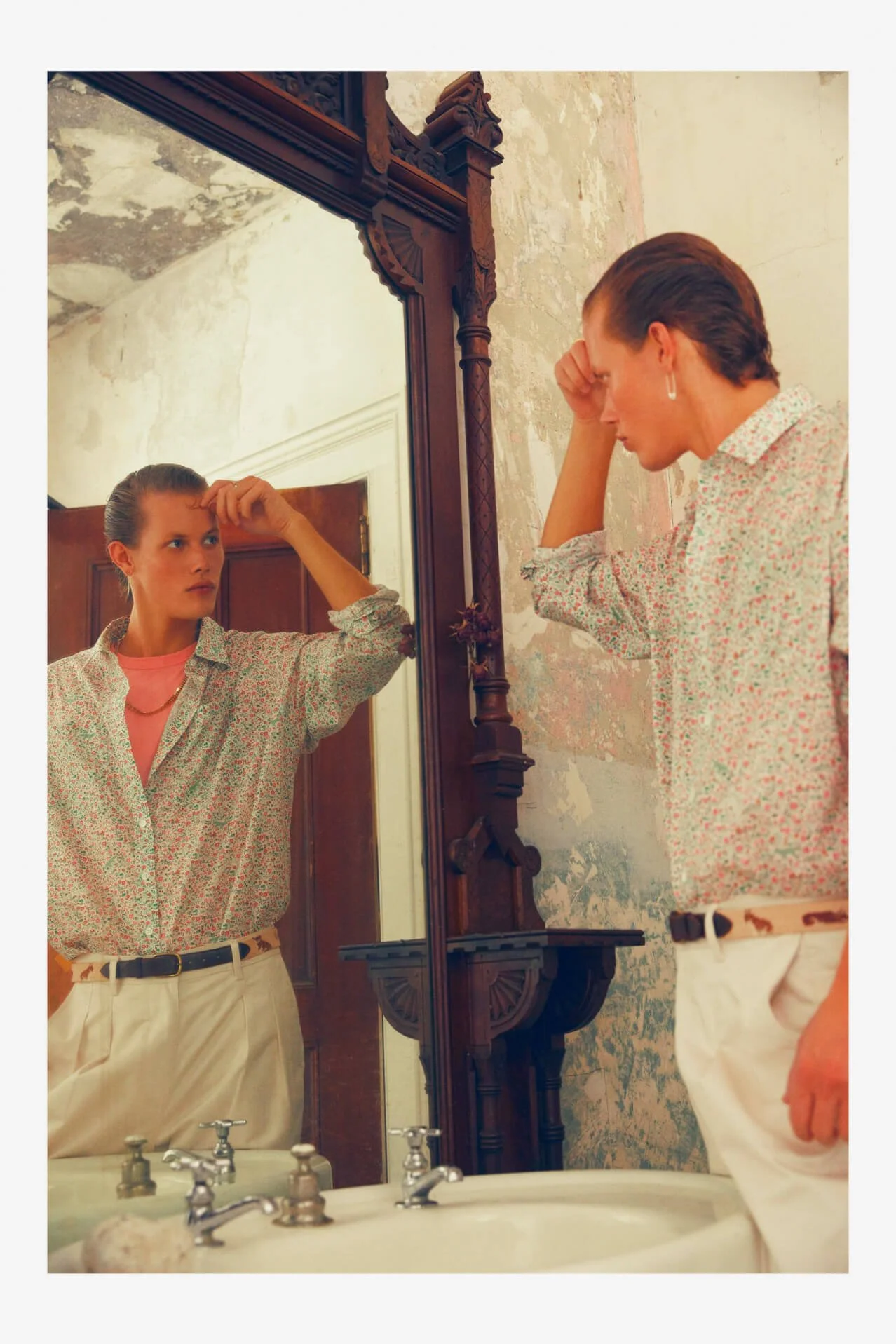 A woman looking at her reflection in a mirror, with a distressed or contemplative expression, in a bathroom with weathered walls.