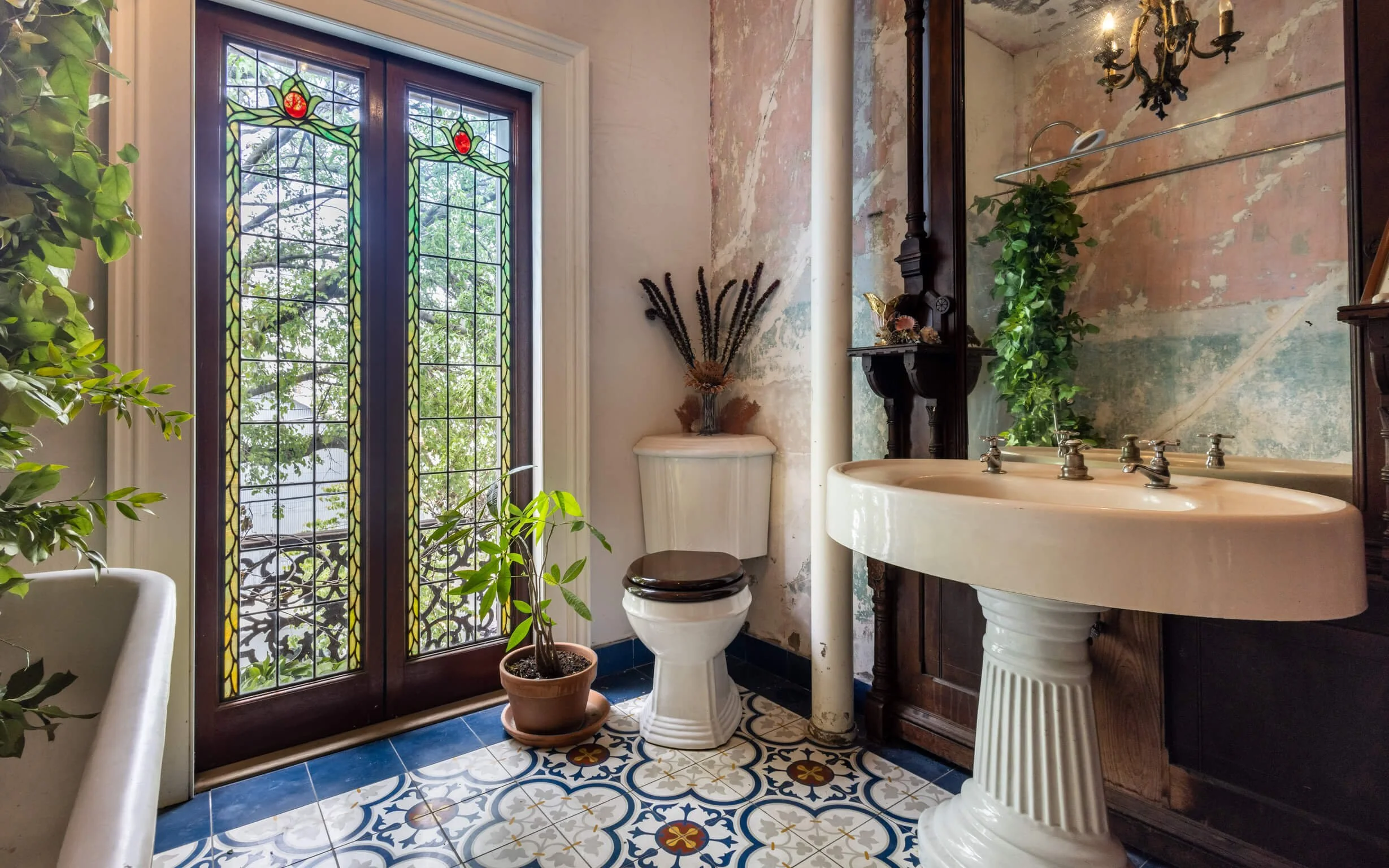 Vintage bathroom with stained glass doors, a vintage toilet, a pedestal sink, and greenery.
