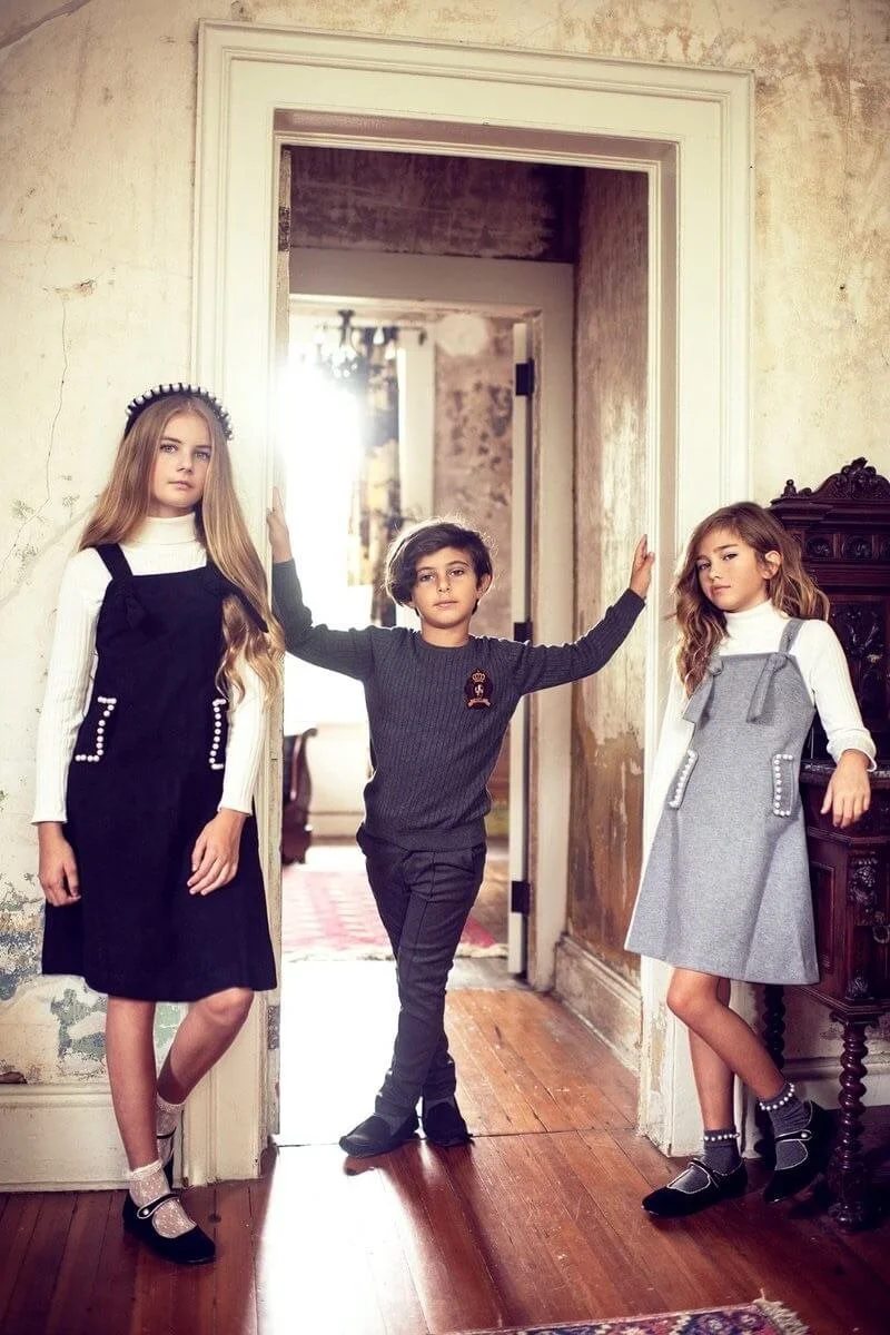 Three children standing in a doorway of an old, rustic house, with two girls on either side and a boy in the middle, posing for a photo.