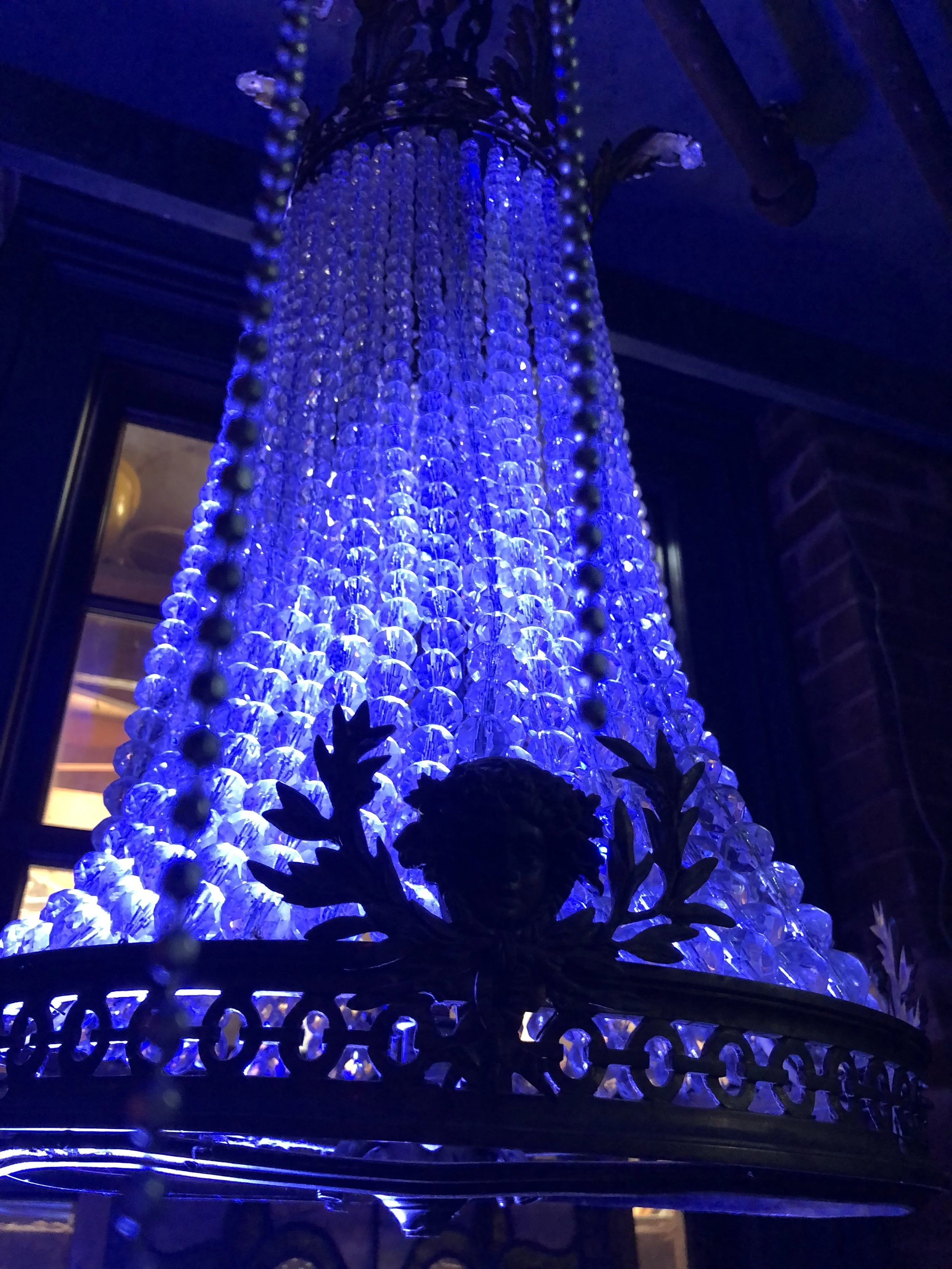 Close-up view of a large, ornate chandelier with blue lighting, featuring numerous crystal beads and metal decorative elements.