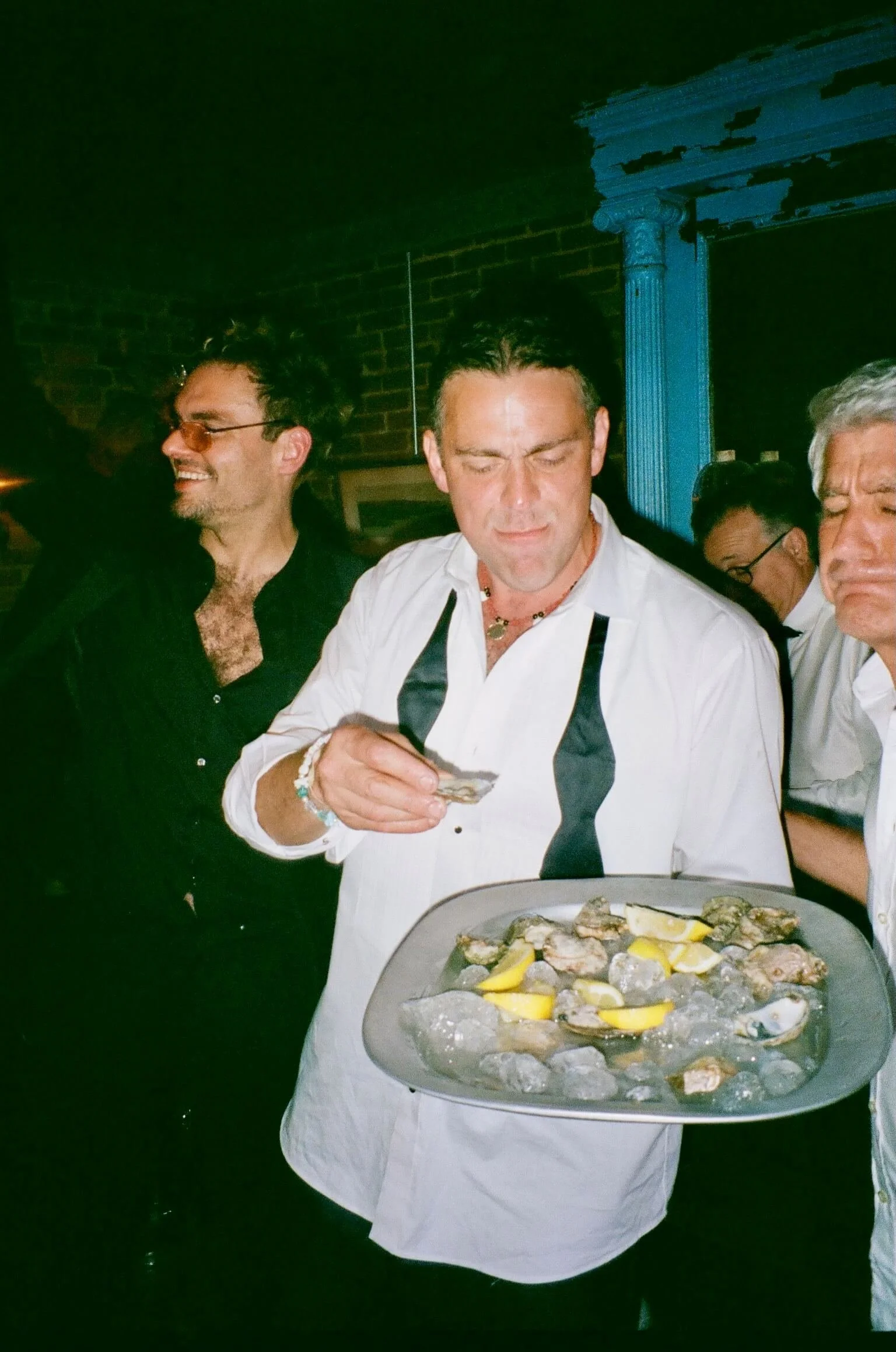A chef holding a tray of oysters garnished with lemon wedges at a restaurant or bar.