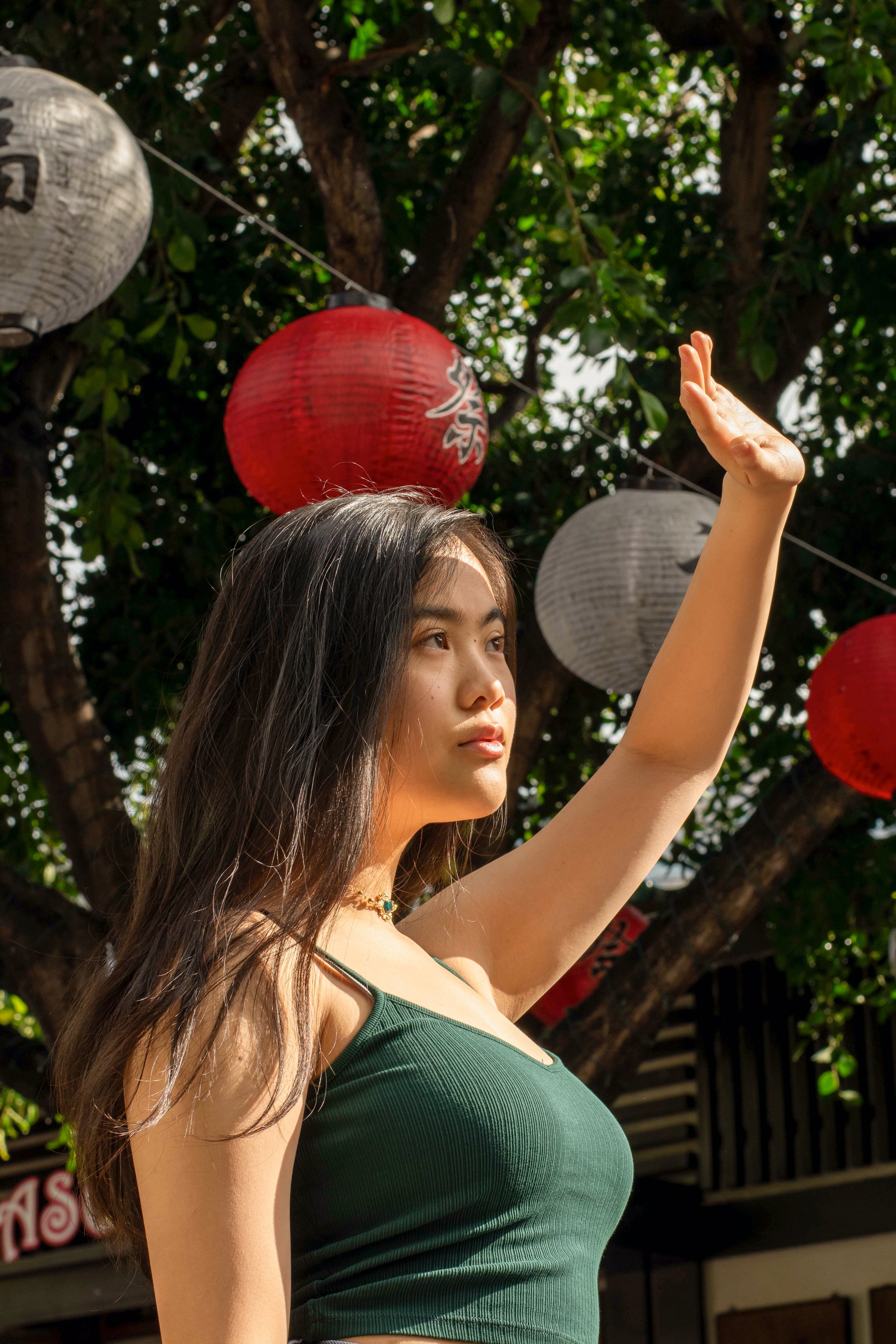 Woman in green top shielding eyes outdoors with red and white lanterns hanging in background.