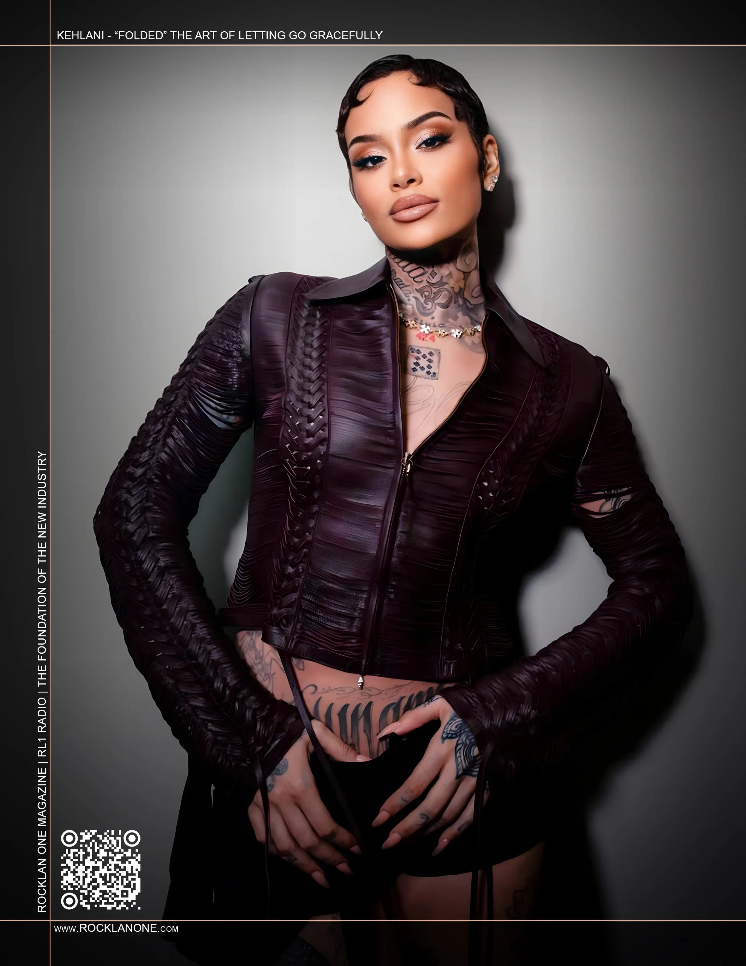 A woman wearing an oversized brown leather coat, with a light pink shirt underneath, and pinstriped brown pants. She has short black hair, tattoos on her neck and torso, and is standing outdoors with a dark background.