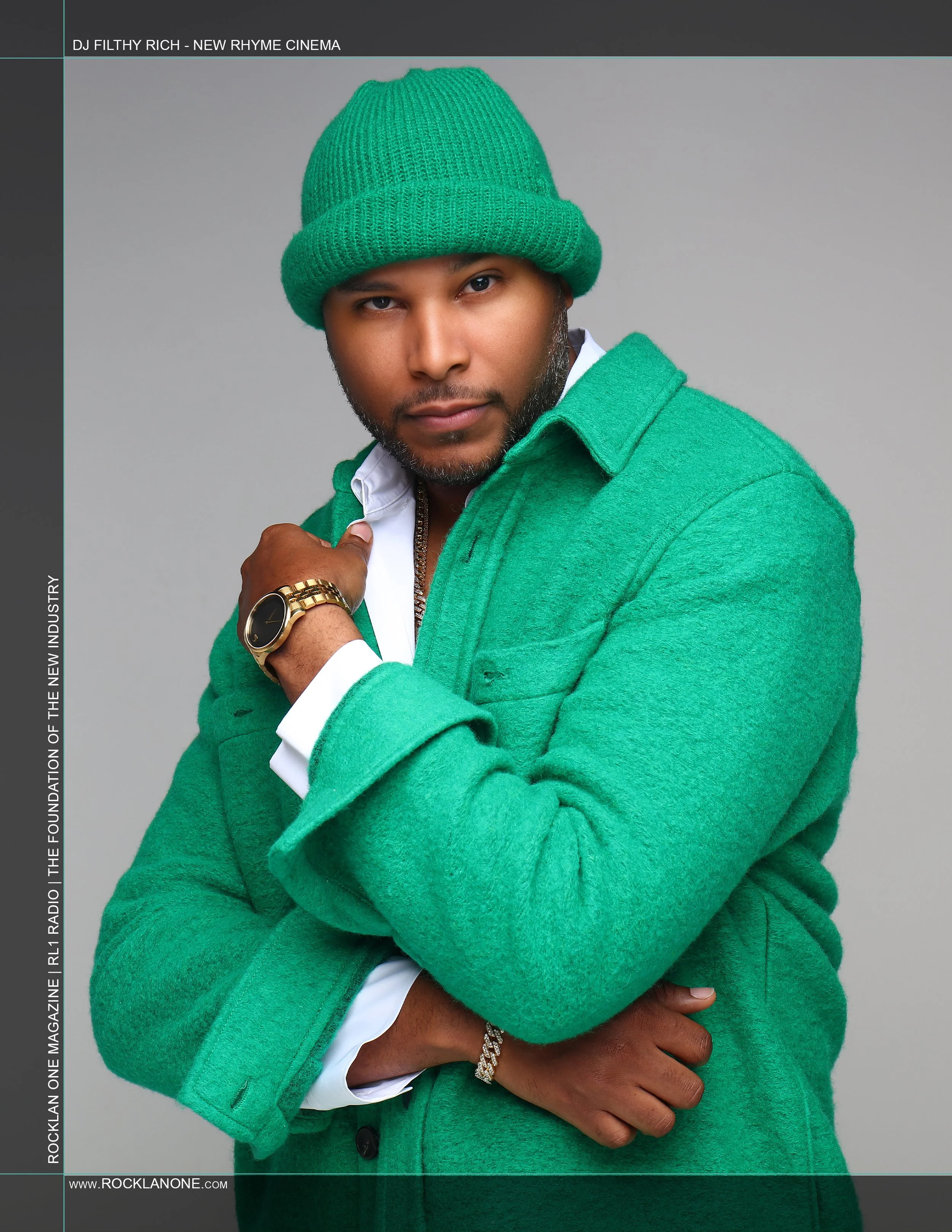 A man wearing a green beanie, green coat, and white shirt, accessorized with a gold watch and bracelet, posing against a gray background in a magazine cover photo.
