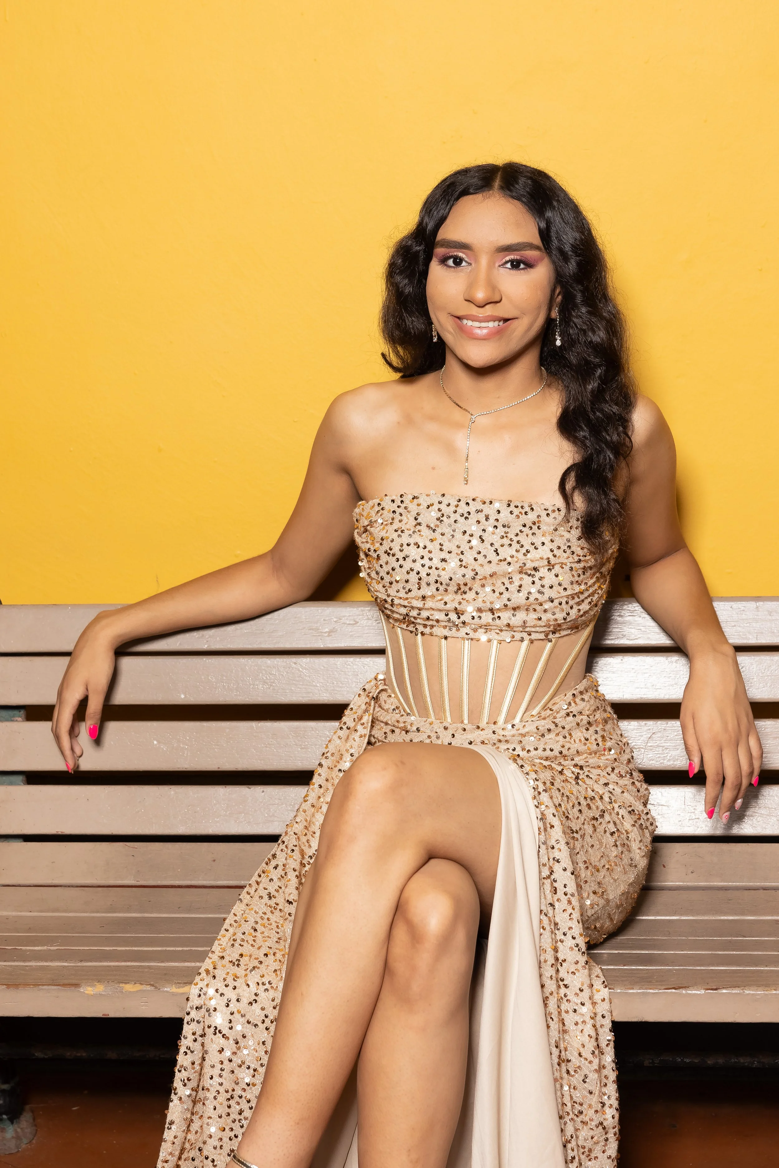 Joven mujer con vestido elegante sentado en un banco, sonriendo, fondo amarillo.