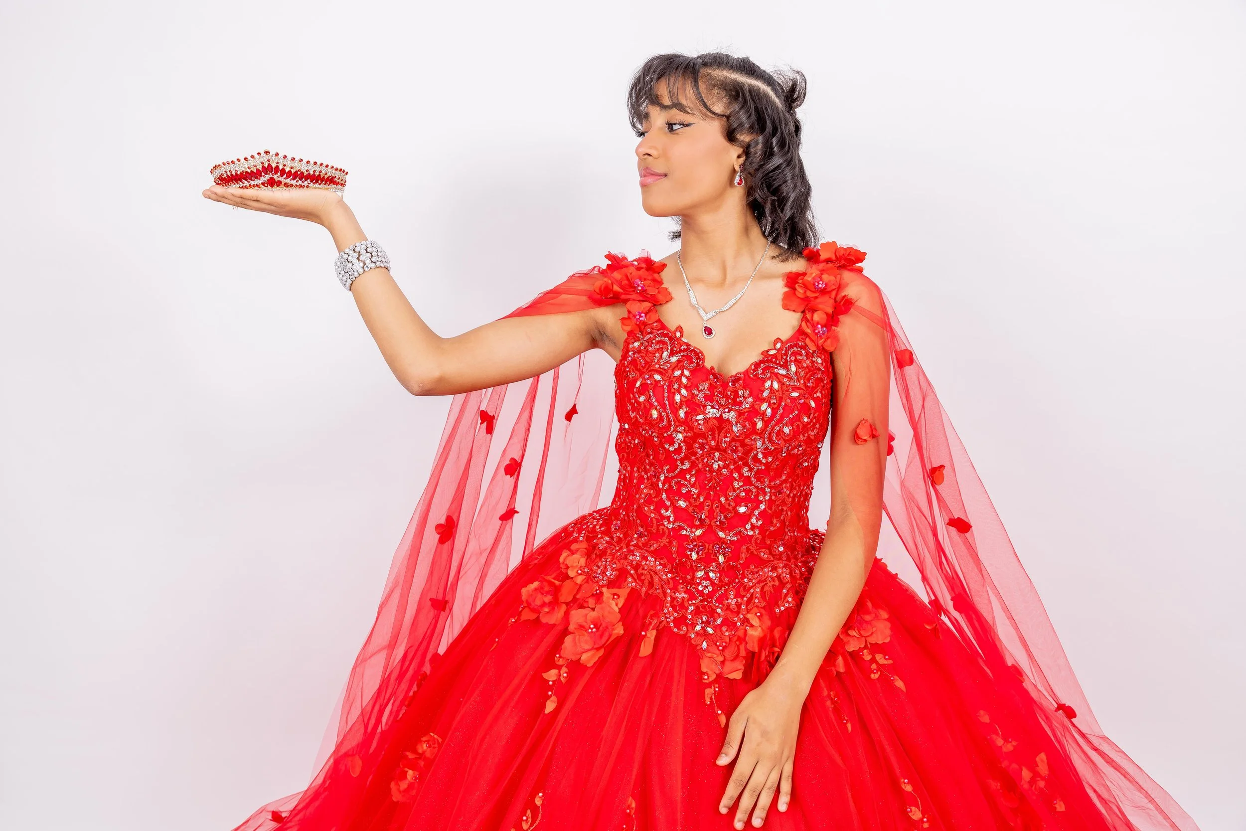 Joven mujer con vestido de novia rojo y accesorios, sosteniendo una corona en la mano extendida.