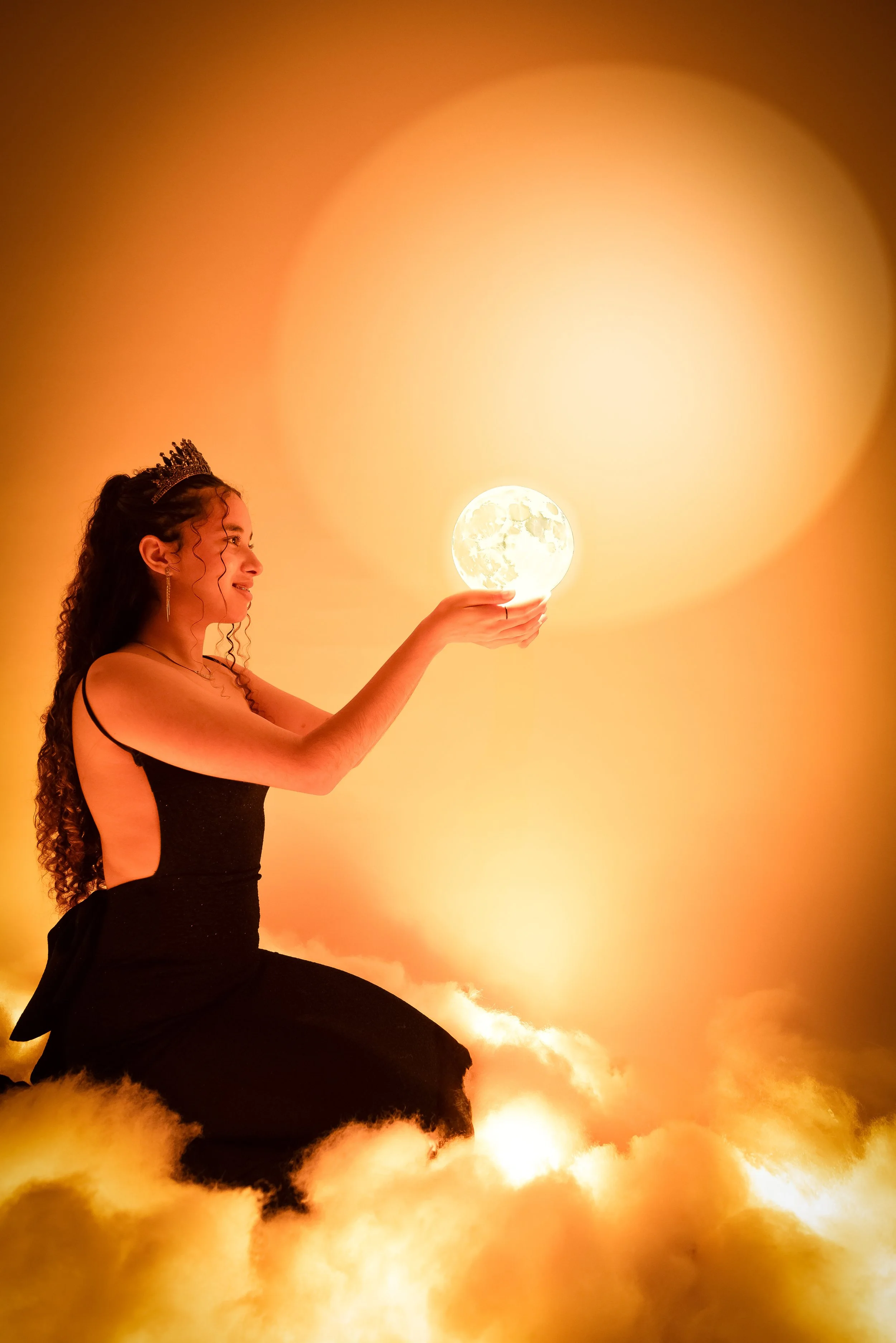 Una mujer con corona sostiene una luna llena en la mano, rodeada de nubes doradas y un fondo brillante.