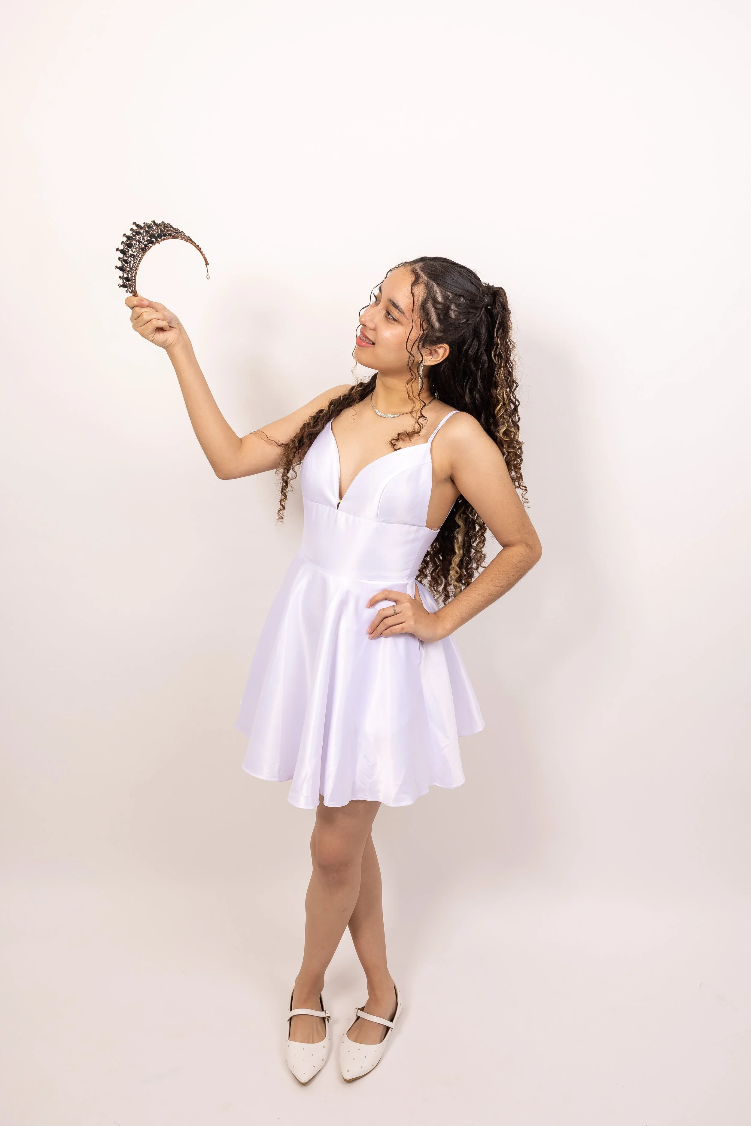 Joven mujer con vestido blanco sosteniendo una diadema en un fondo blanco.